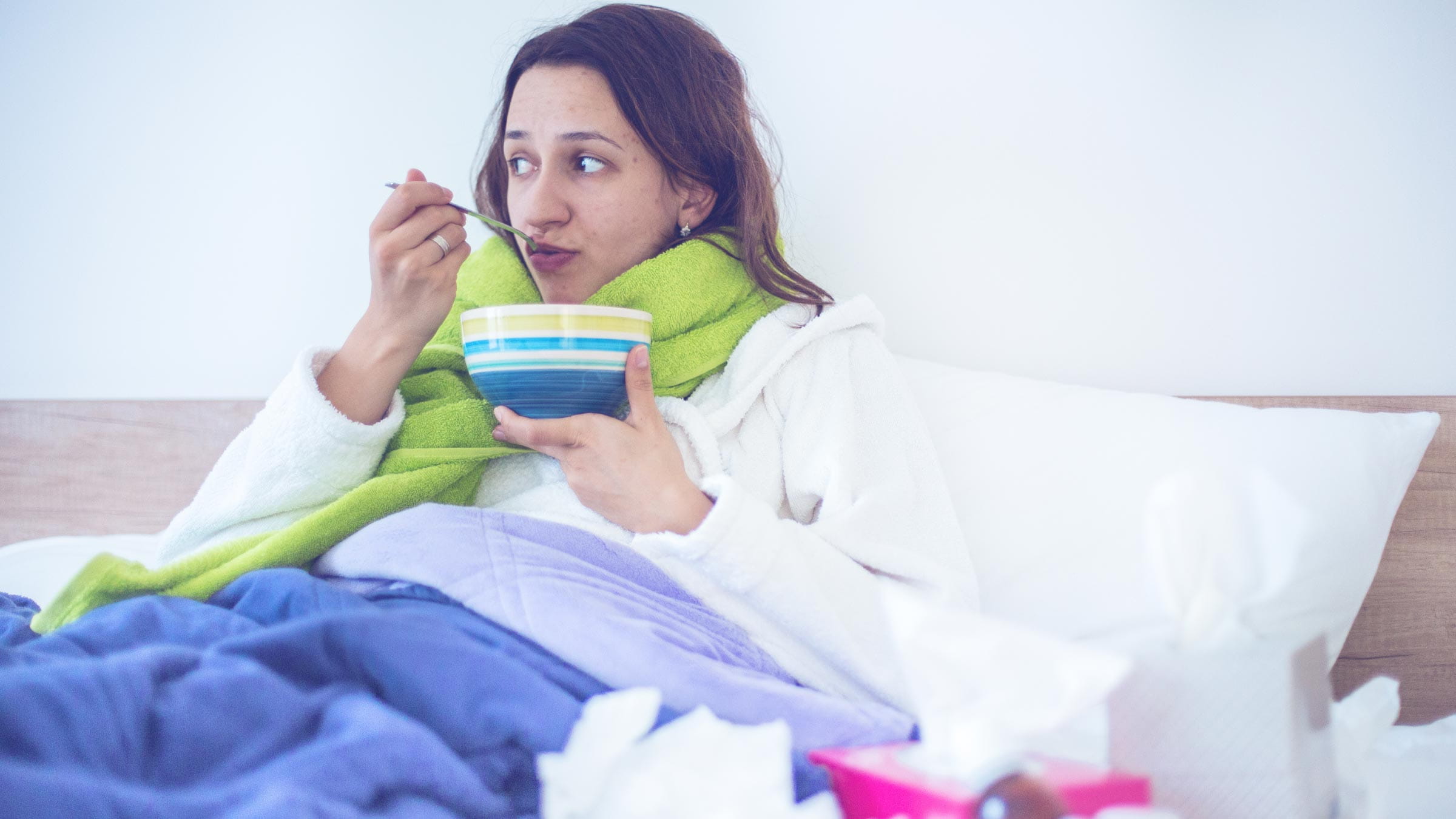 Woman laying in bed eating a bowl of soup