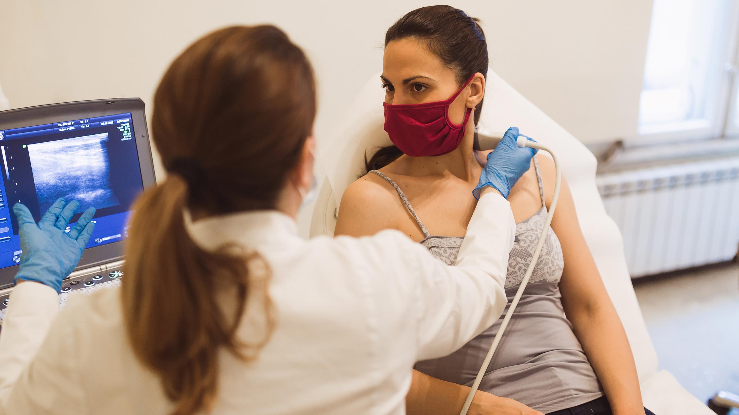 Doctor giving a young female patient an ultrasound of the thyroid gland
