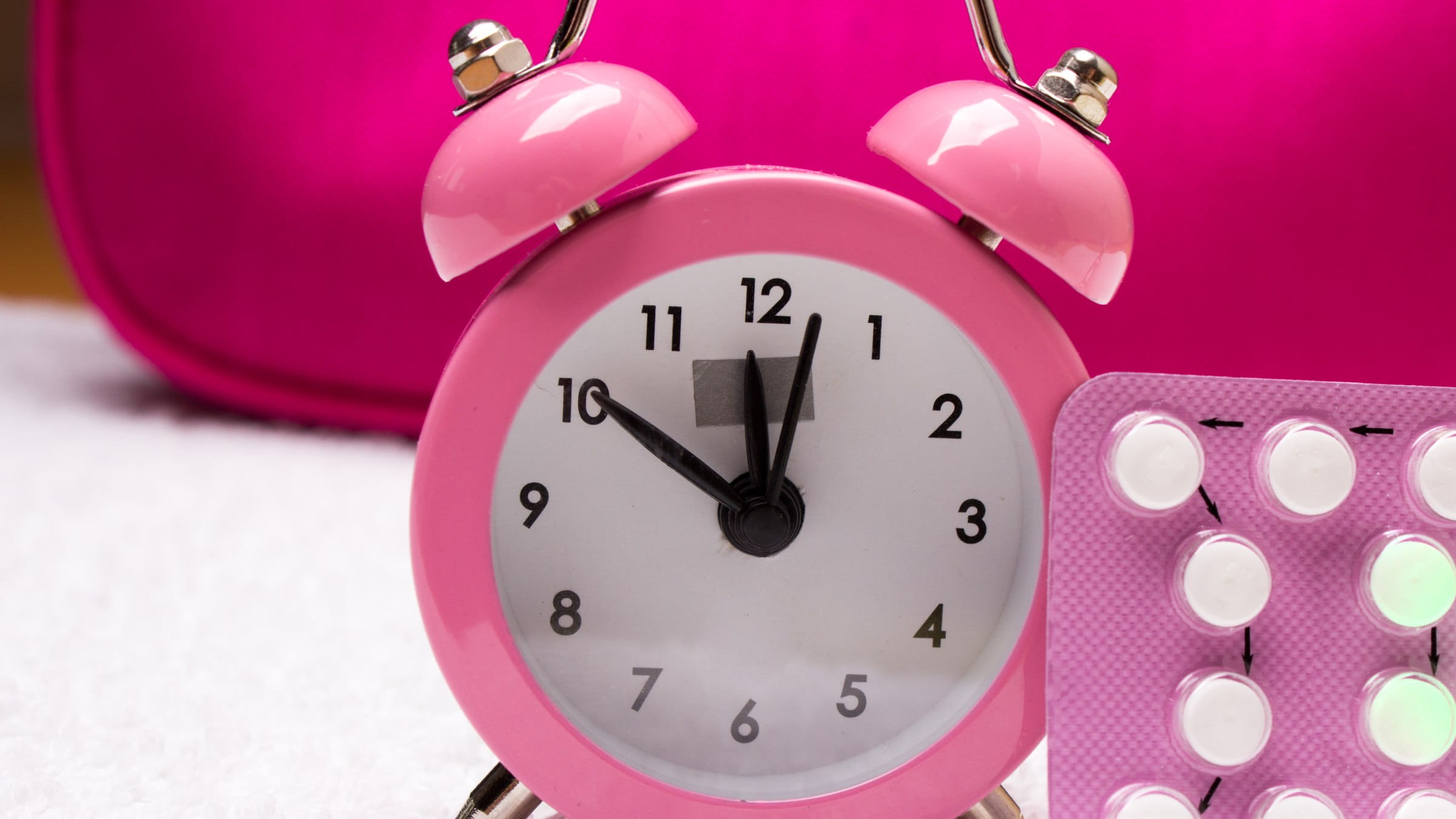 Pink alarm clock with a pink packet of pills