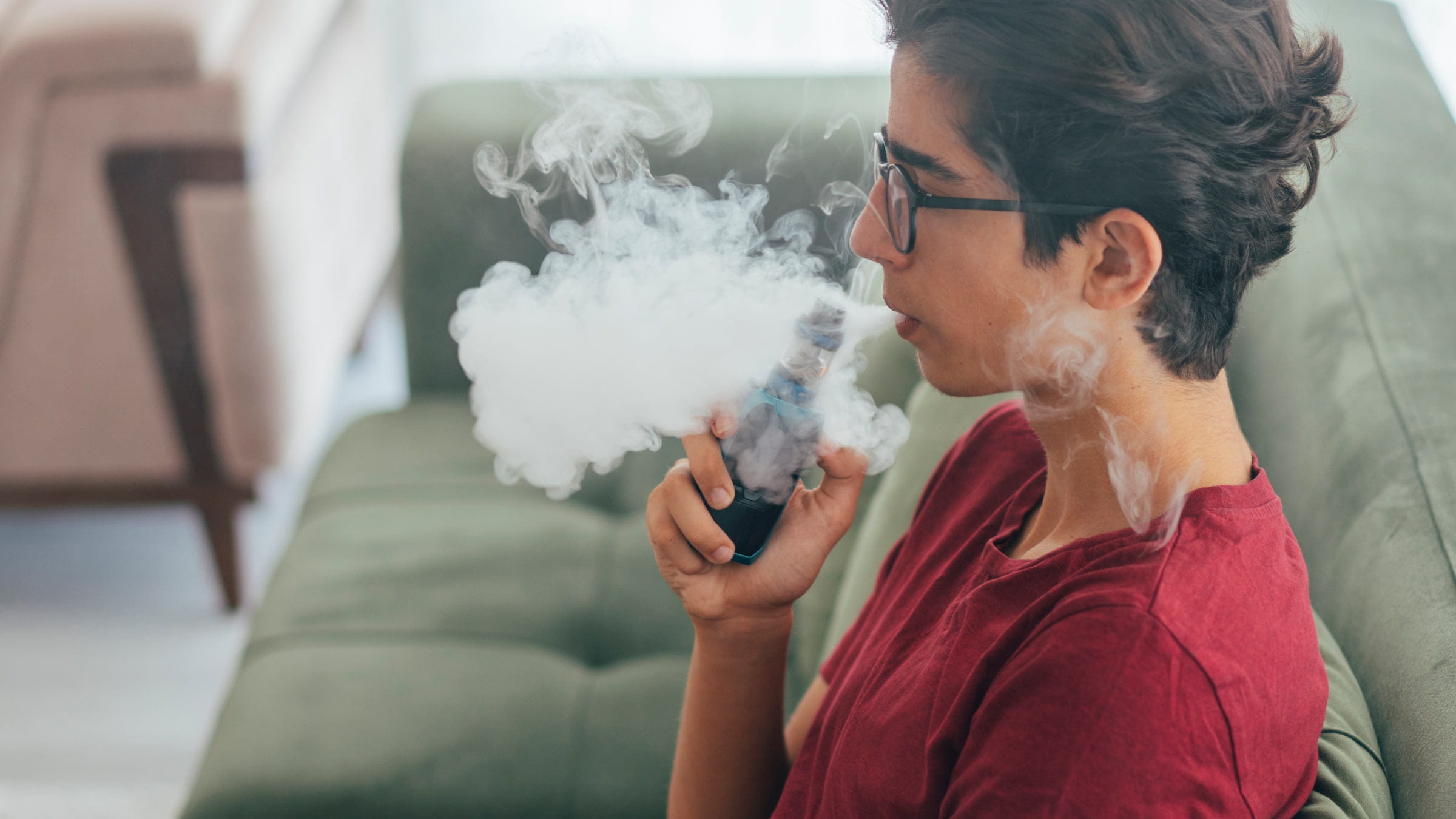 Teenage boy vaping e-cigarette at home