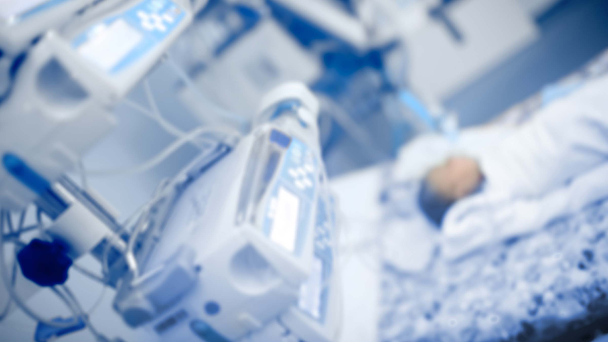 Baby in perinatal hospital care bed surrounded by hospital machinery.