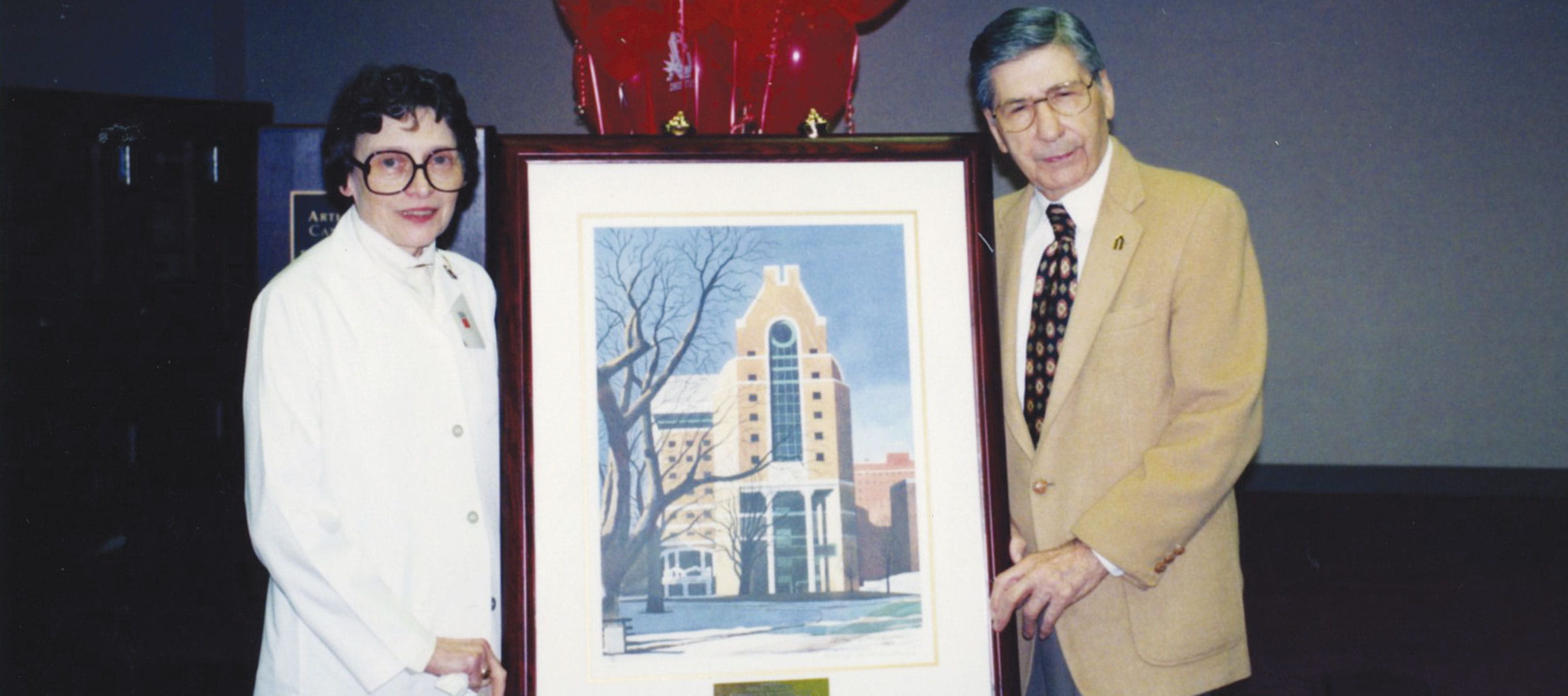 Arthur G. James, MD and Norma Flesher holding a framed image of the original cancer hospital.