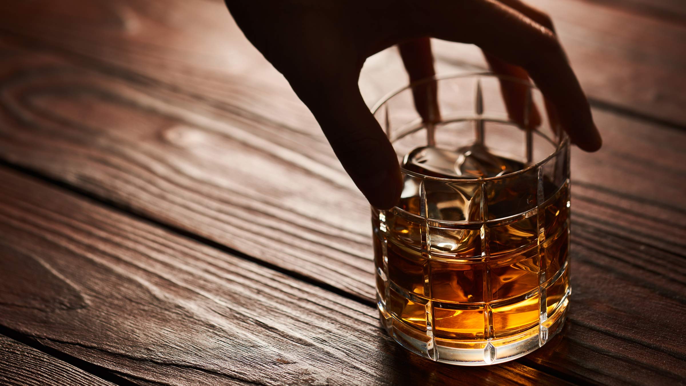 Man's hand reaching for a glass of whiskey on ice