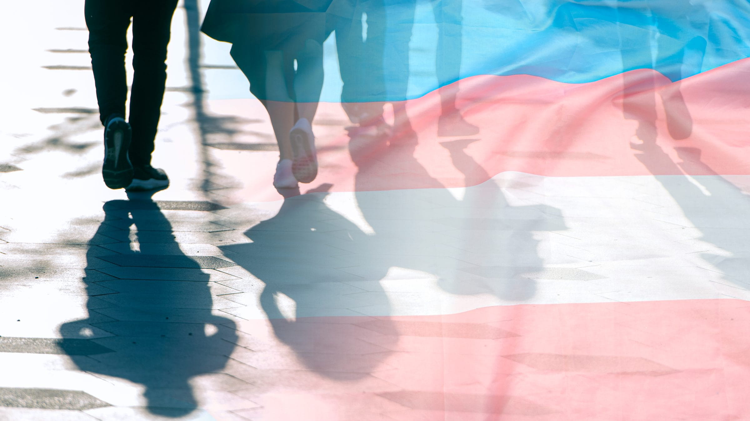 People's feet walking with the trans flag on the foreground