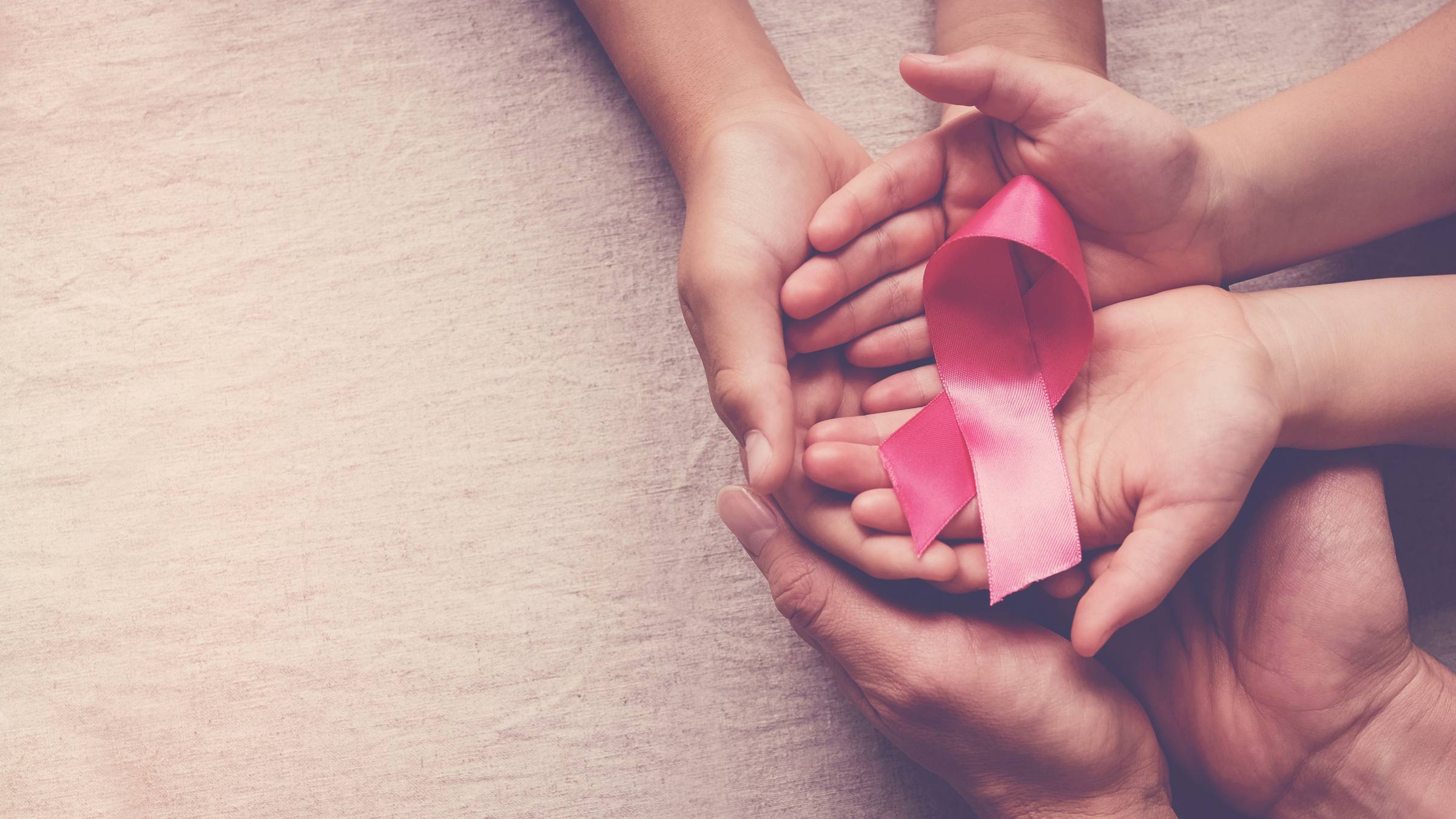 Close-up of hands holding a pink ribbon