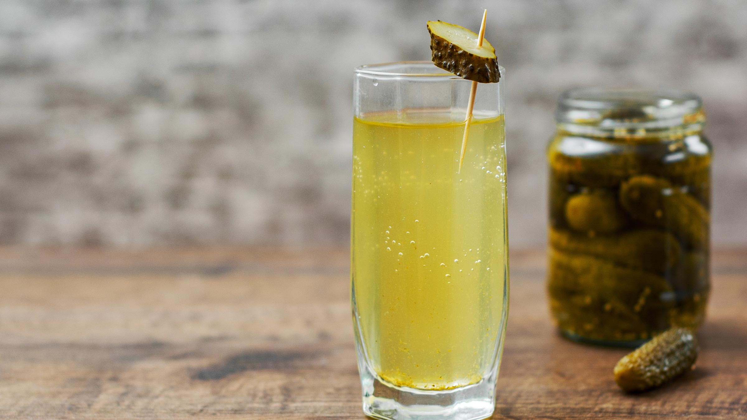 Pickle juice in a glass with an opened jar of pickles nearby
