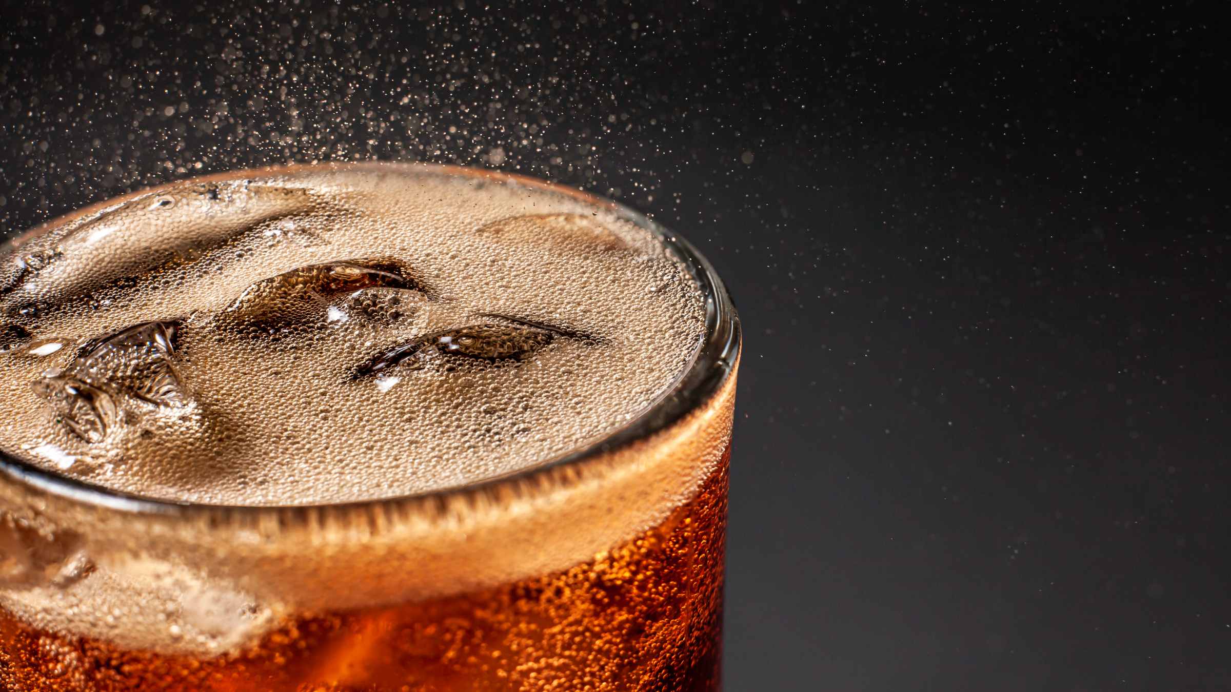 A close-up picture of an iced glass of soda and the carbonation bobbles popping