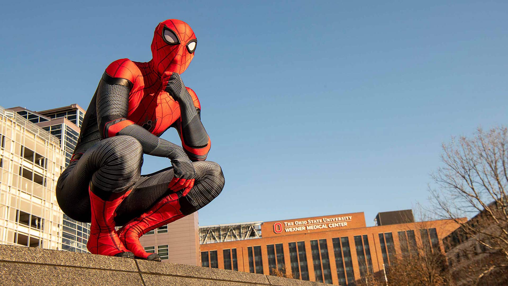 Spider-Man in a squat pose on a wall with The Ohio State Wexner Medical Center building on a background