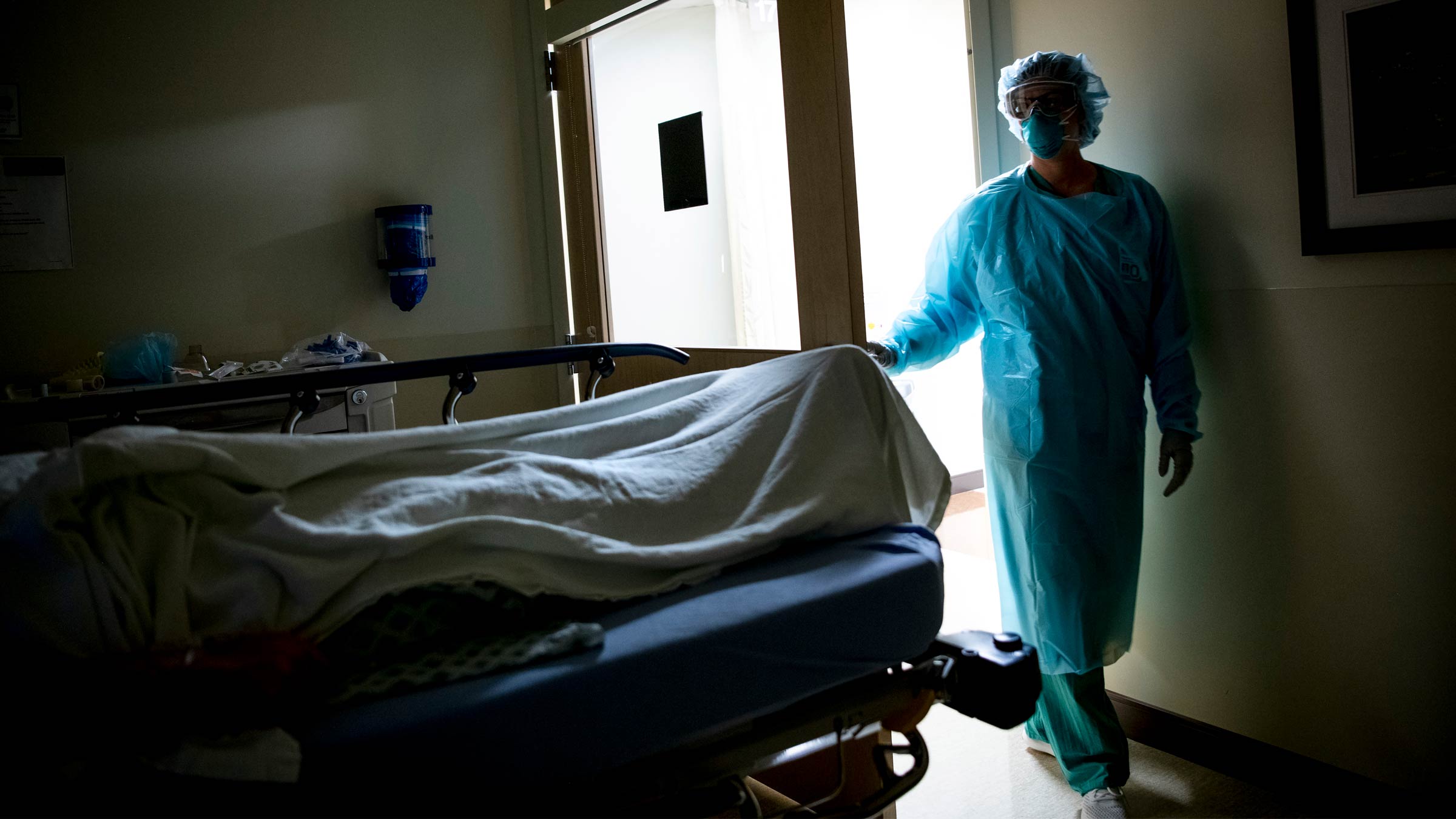 A healthcare worker wearing full PPE walking into a dark hospital room