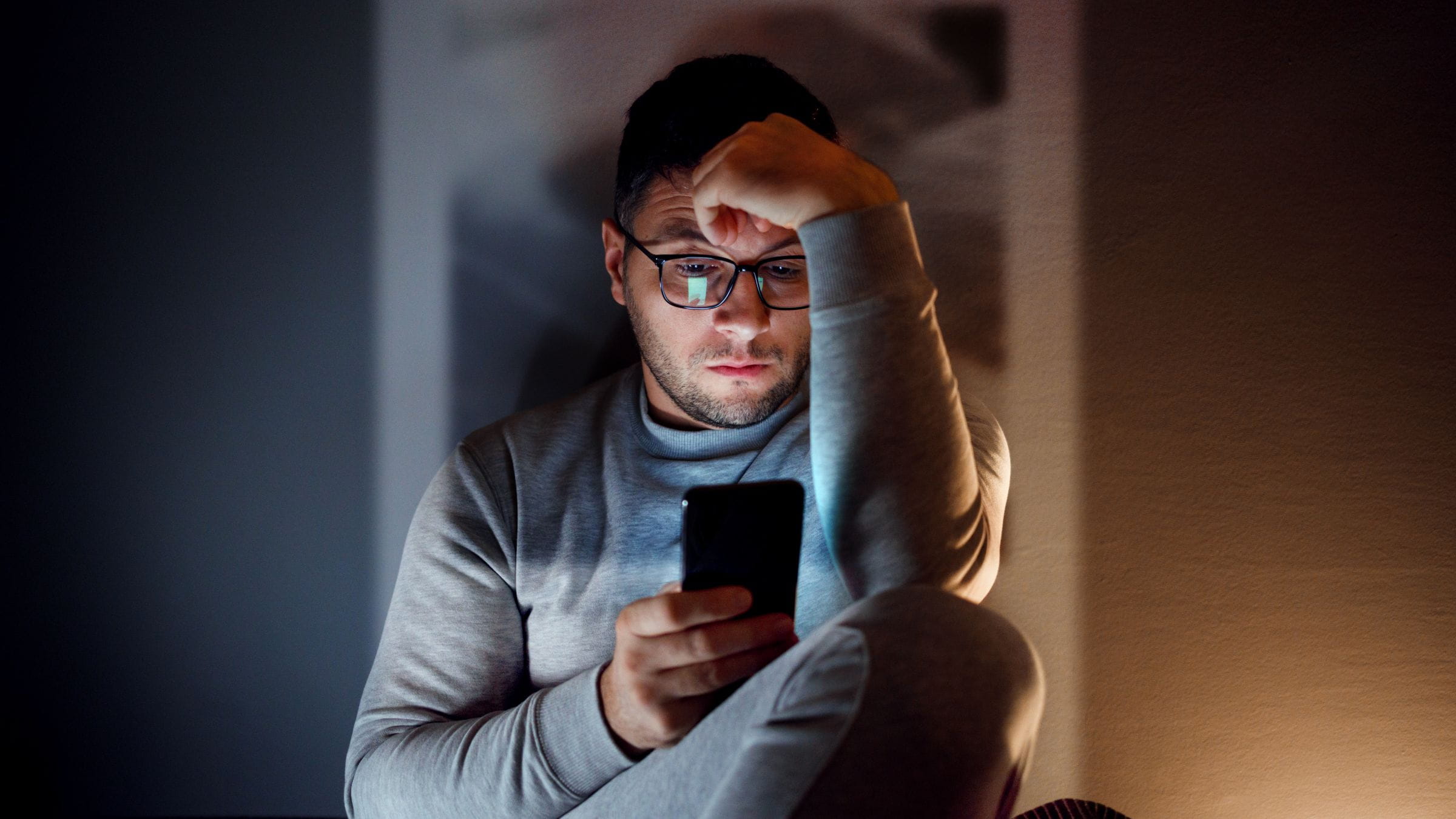 Stressed man sitting in the dark looking at his phone