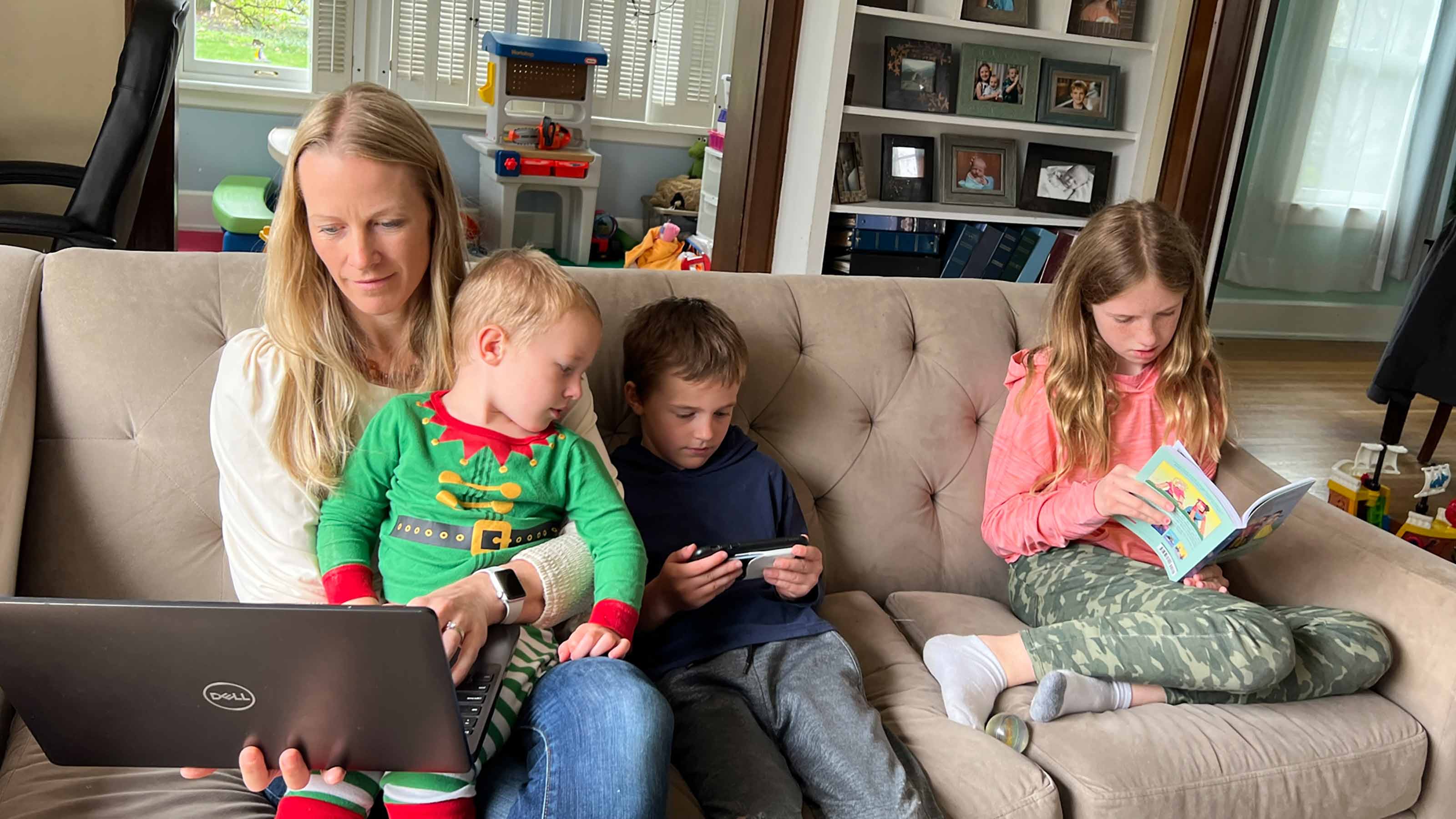 Mother trying to work on a laptop with her three kids on a couch