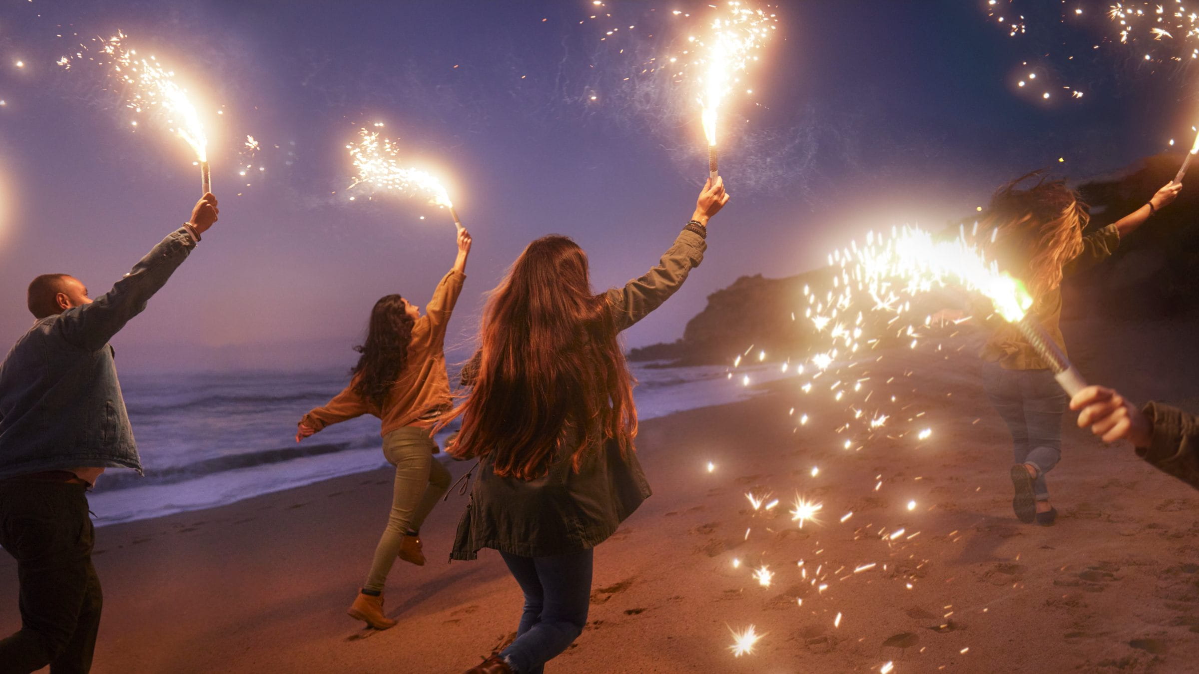 Friends running on the beach holding sparklers