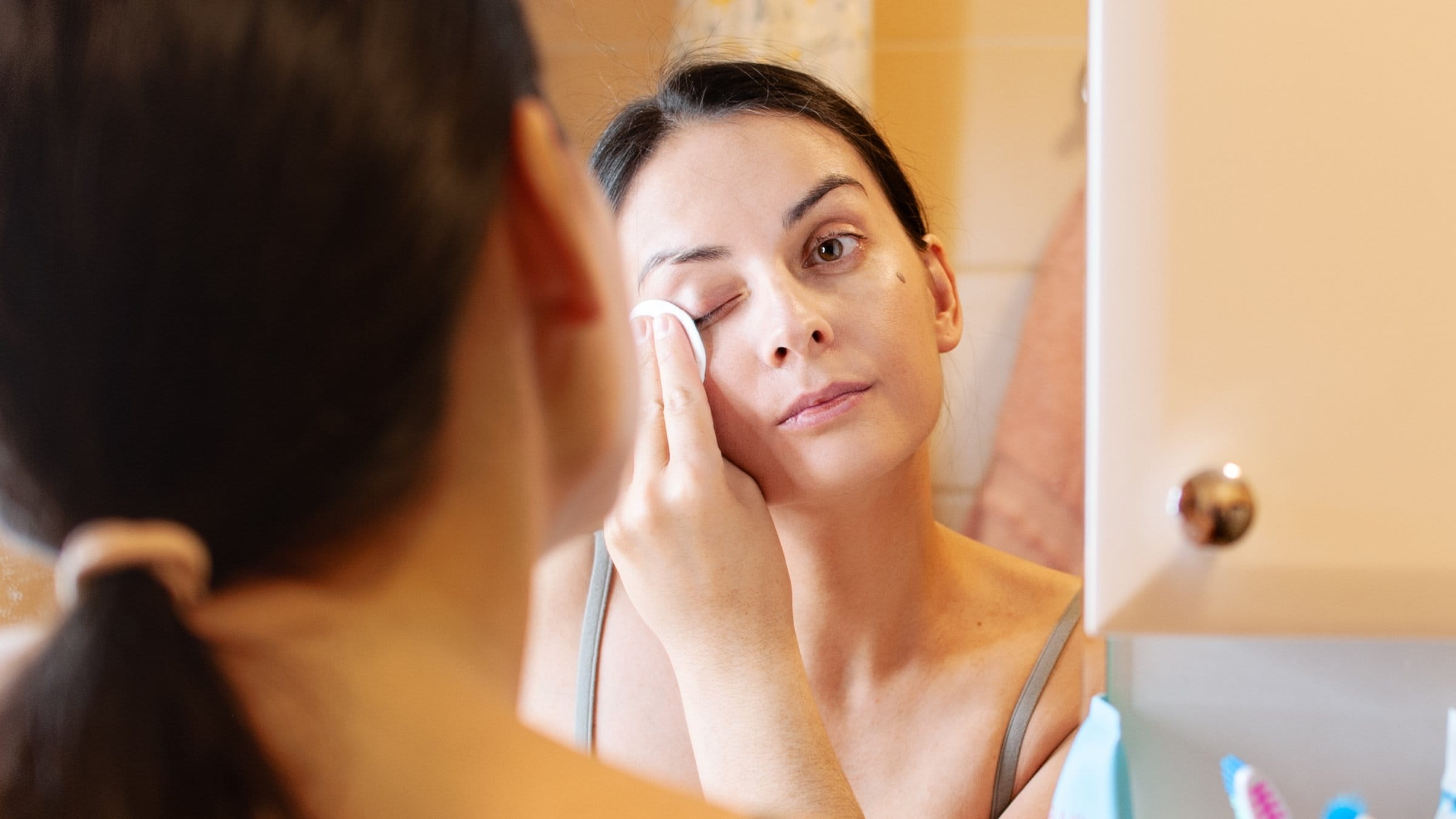 Woman taking off makeup in front of a mirror