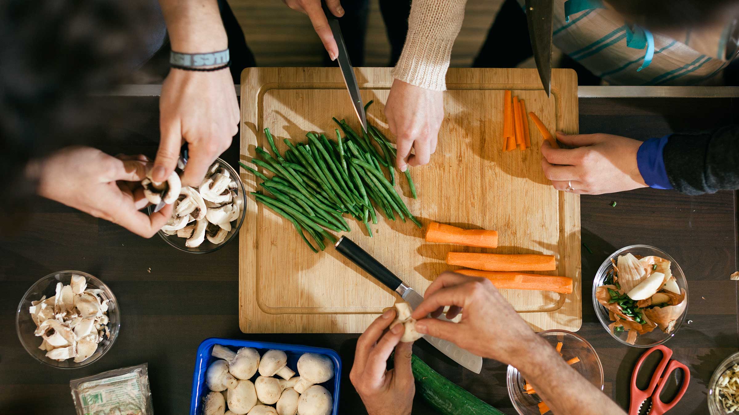 Close up of hands cutting vegetables on a wooden board in cooking class