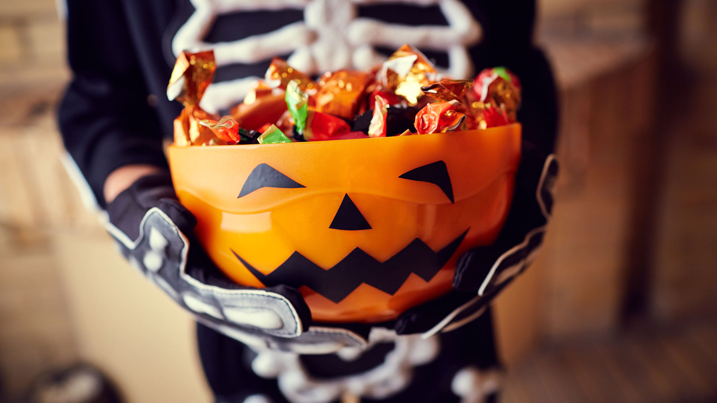 Boy in a skeleton costume holding bowl full of Halloween candy