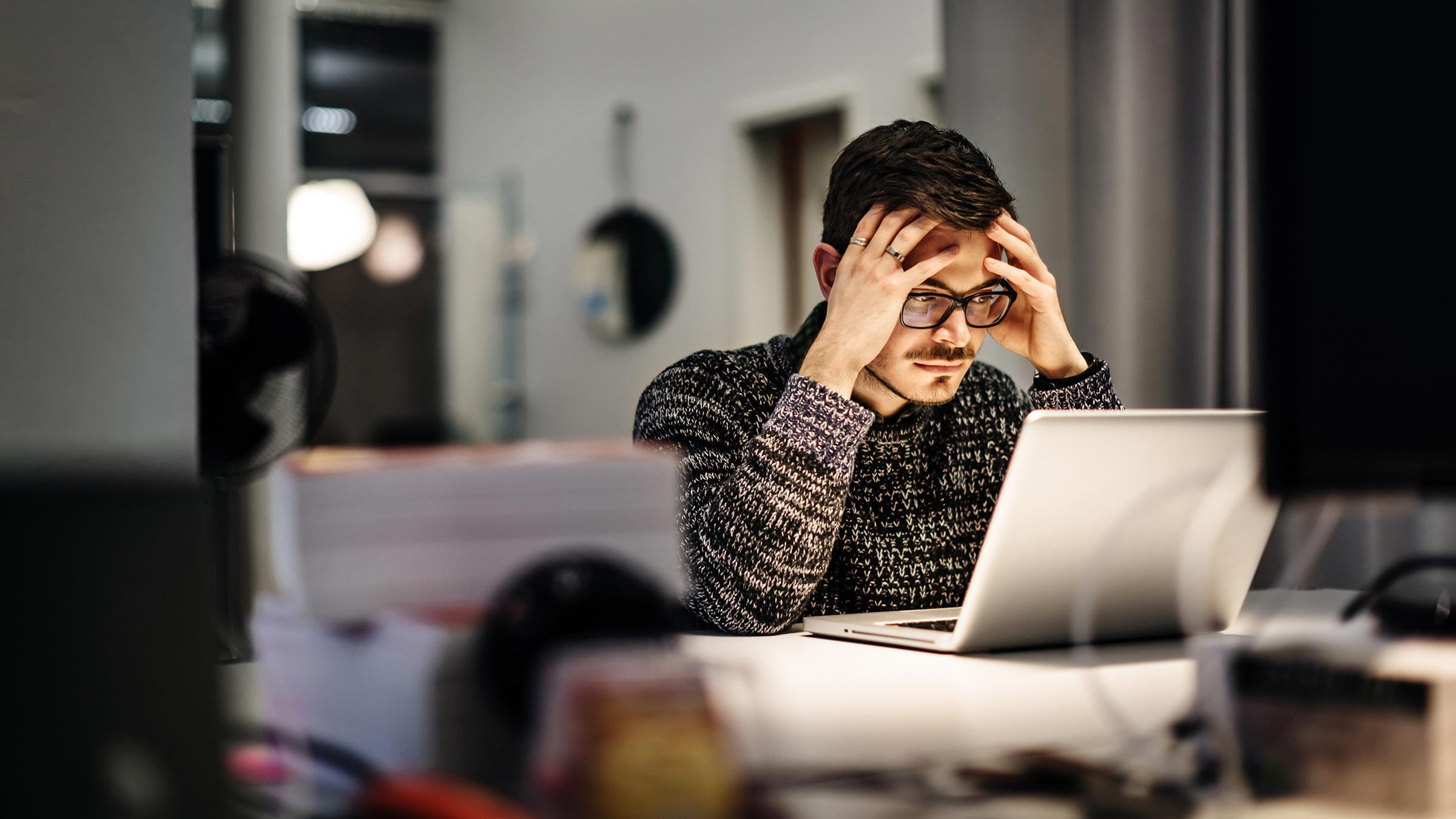 Man holding his head in his hands in front of a laptop