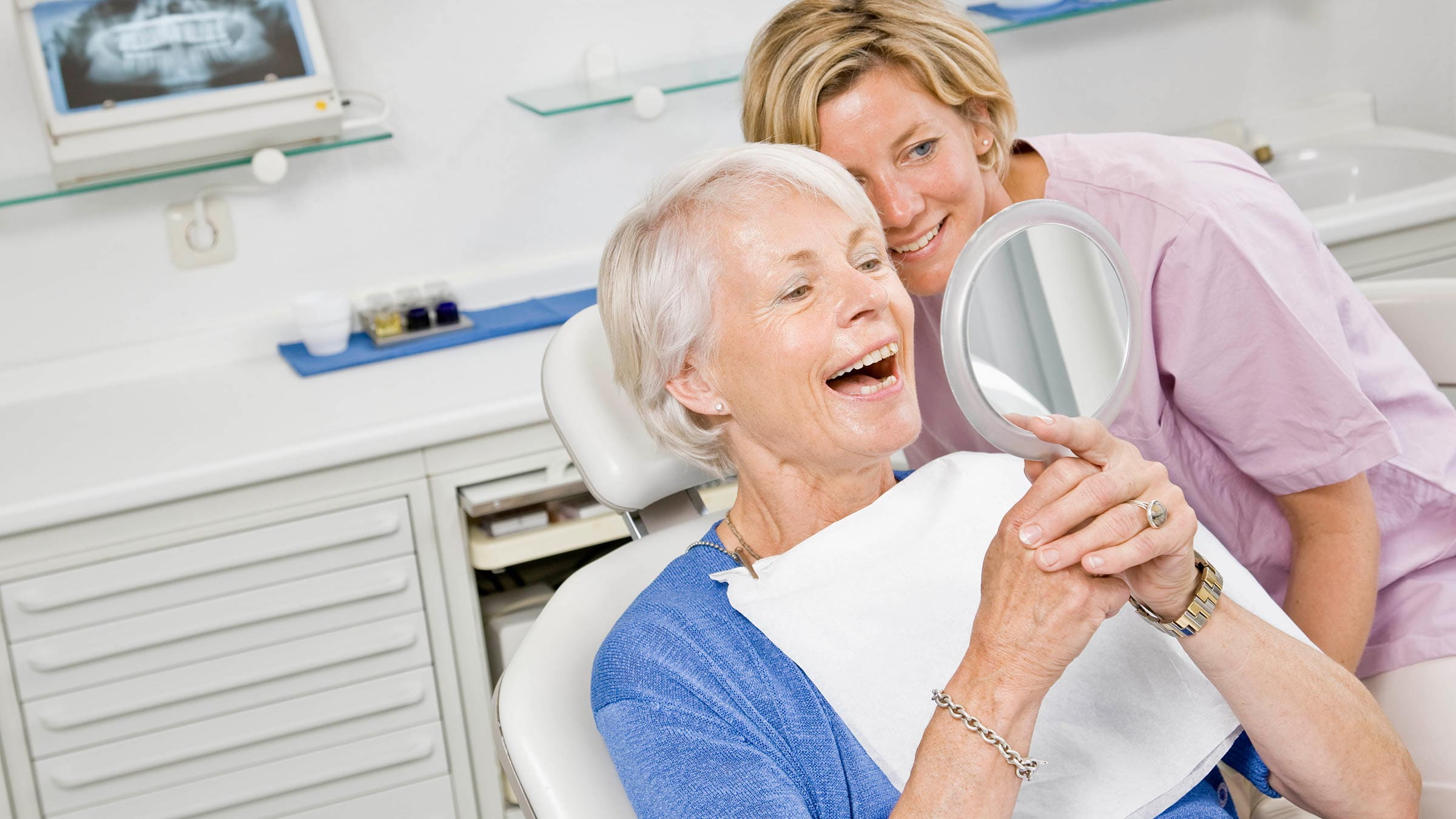 Elderly woman looking in the mirror at her new dental implants