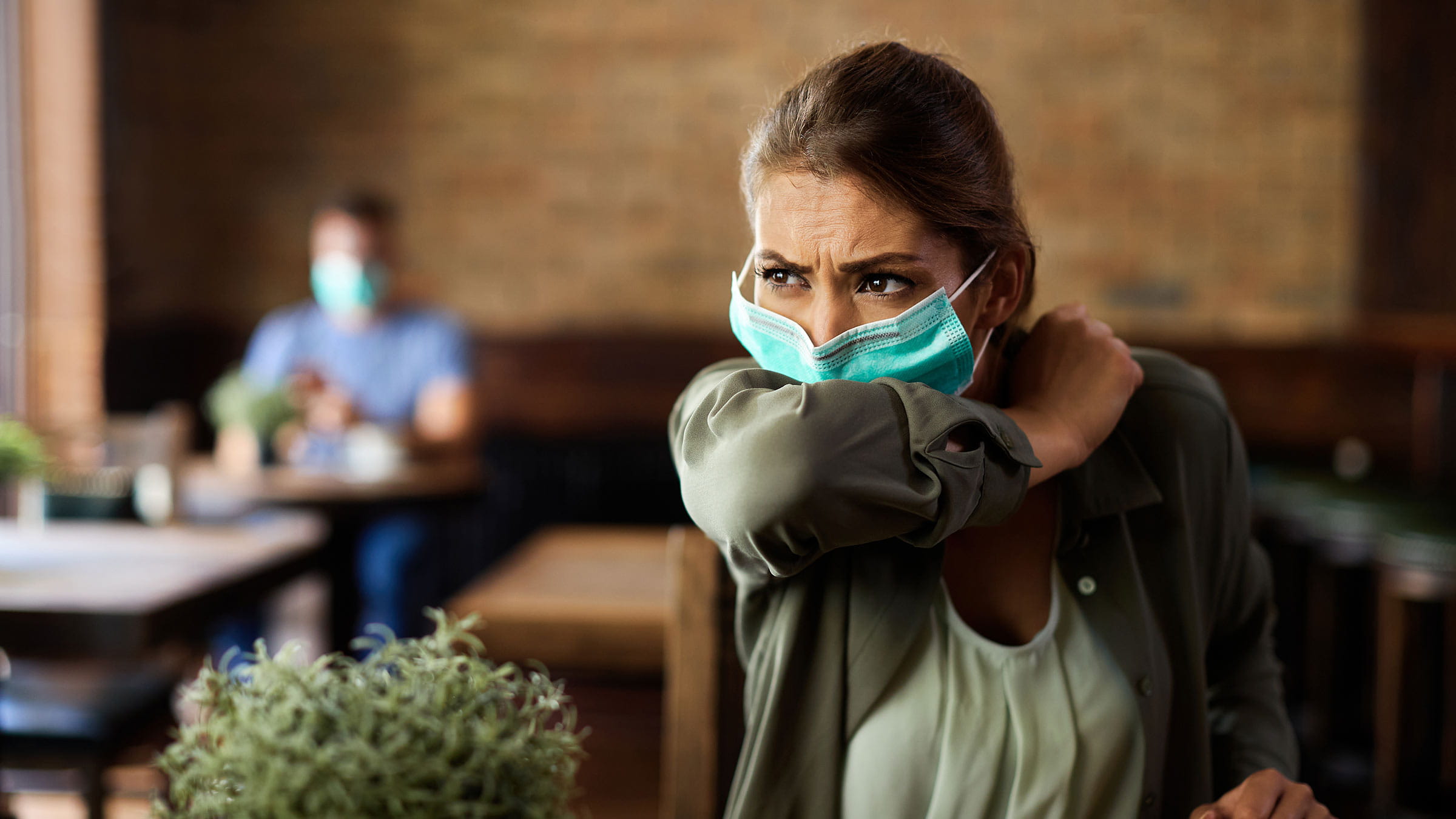 Woman with face mask sneezing into elbow