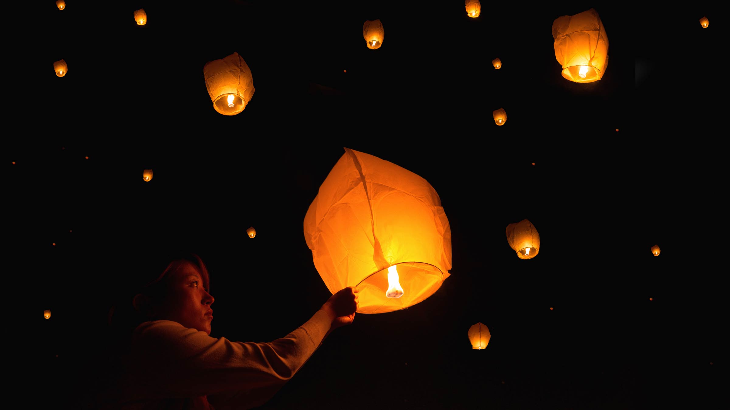 A woman lighting and releasing a paper lantern into the sky