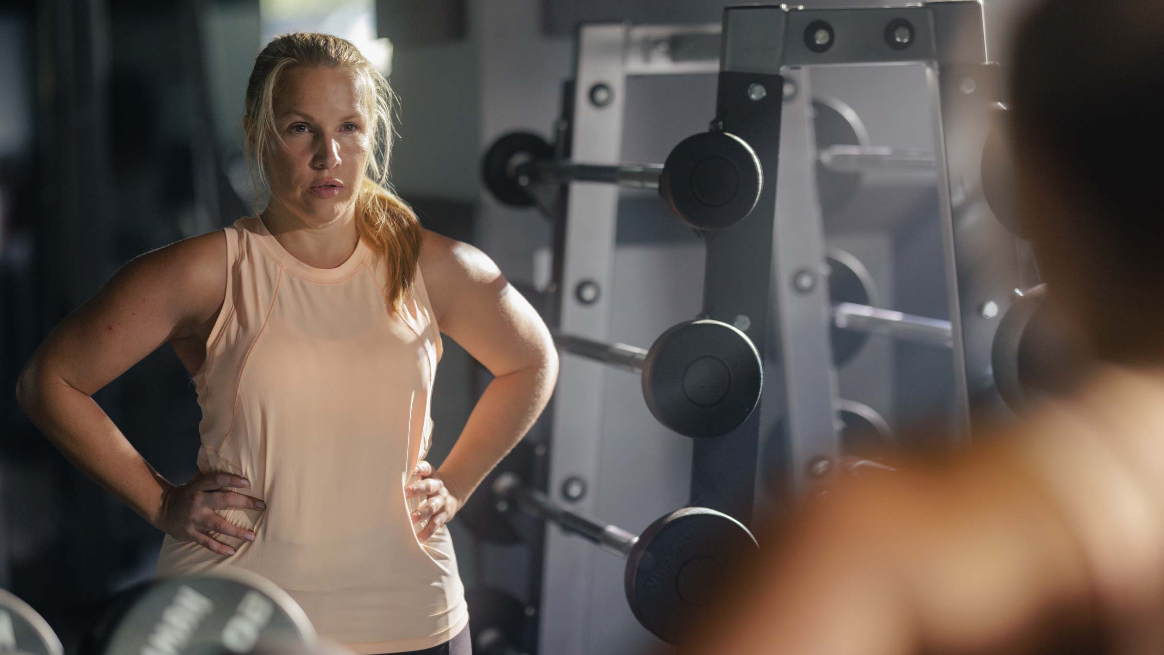 Woman looking in the mirror at the gym with weight rack behind her