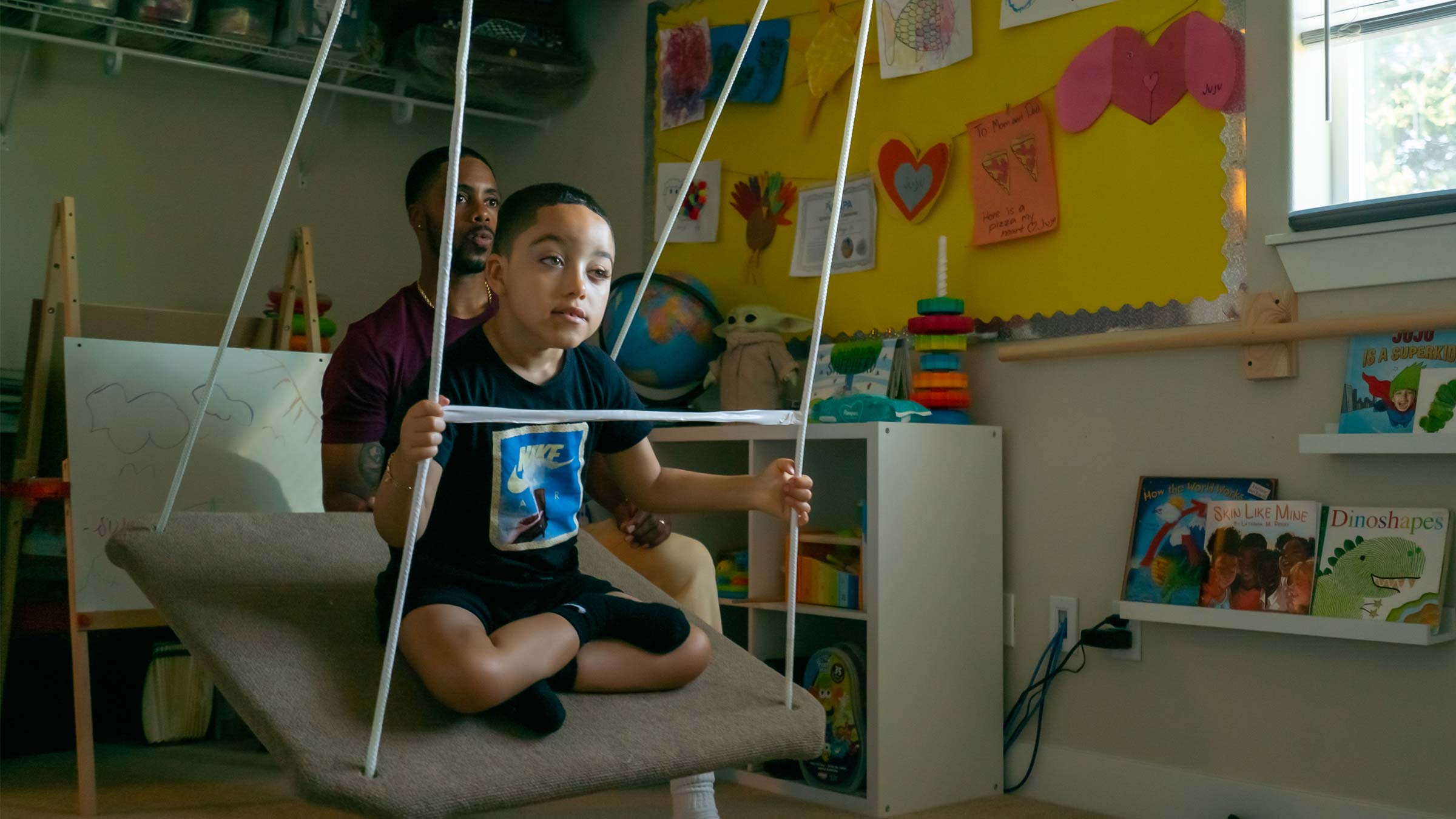 JuJu sits on a swing with his father, Jamell Stagg, in the background