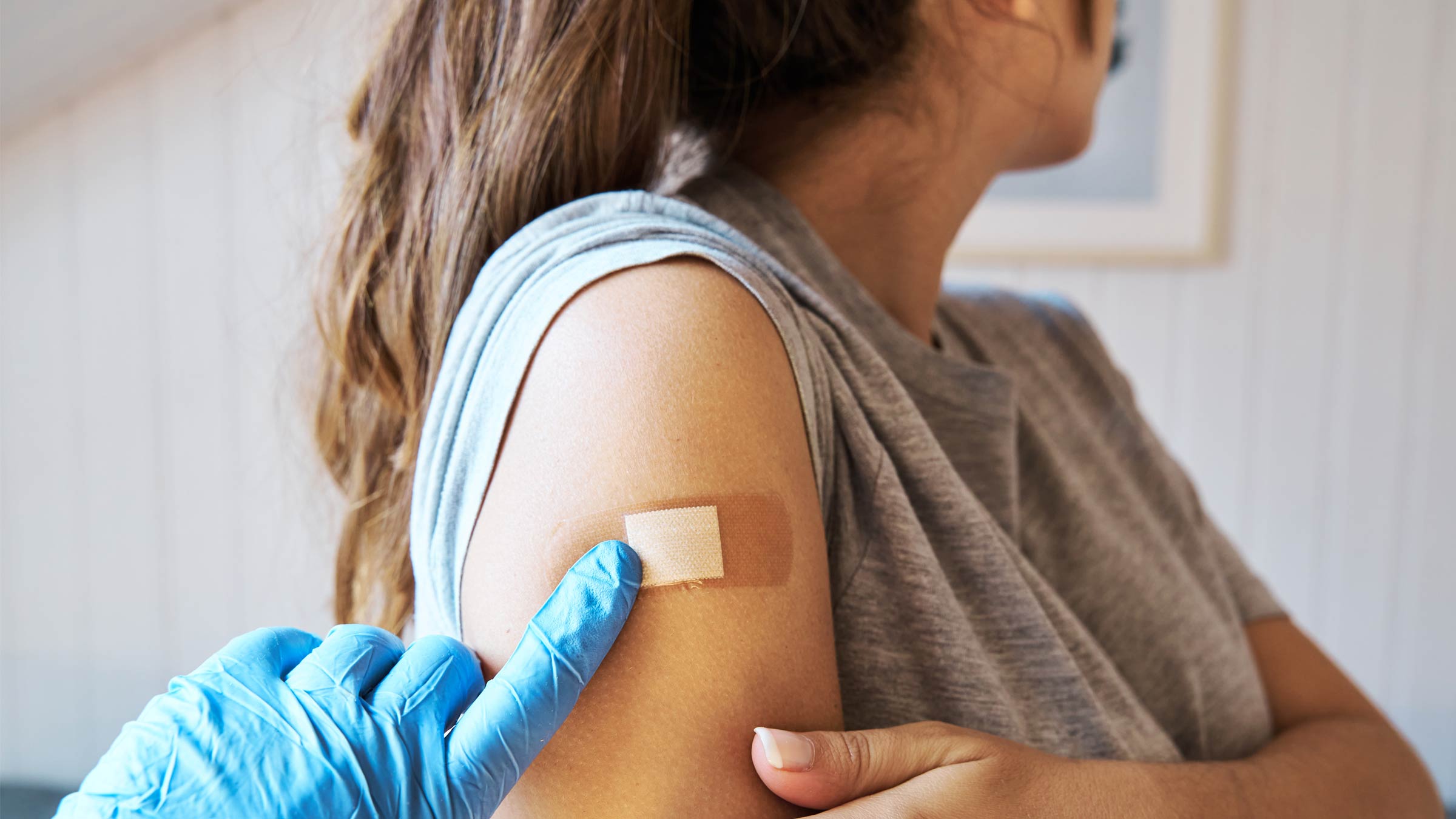 A gloved hand places a bandage on a woman's arm after vaccinating her.