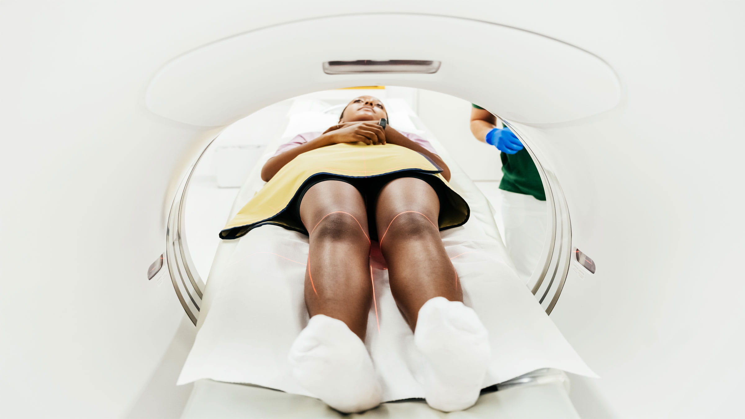 A Black female patient enters an MRI machine lying on her back on a table.