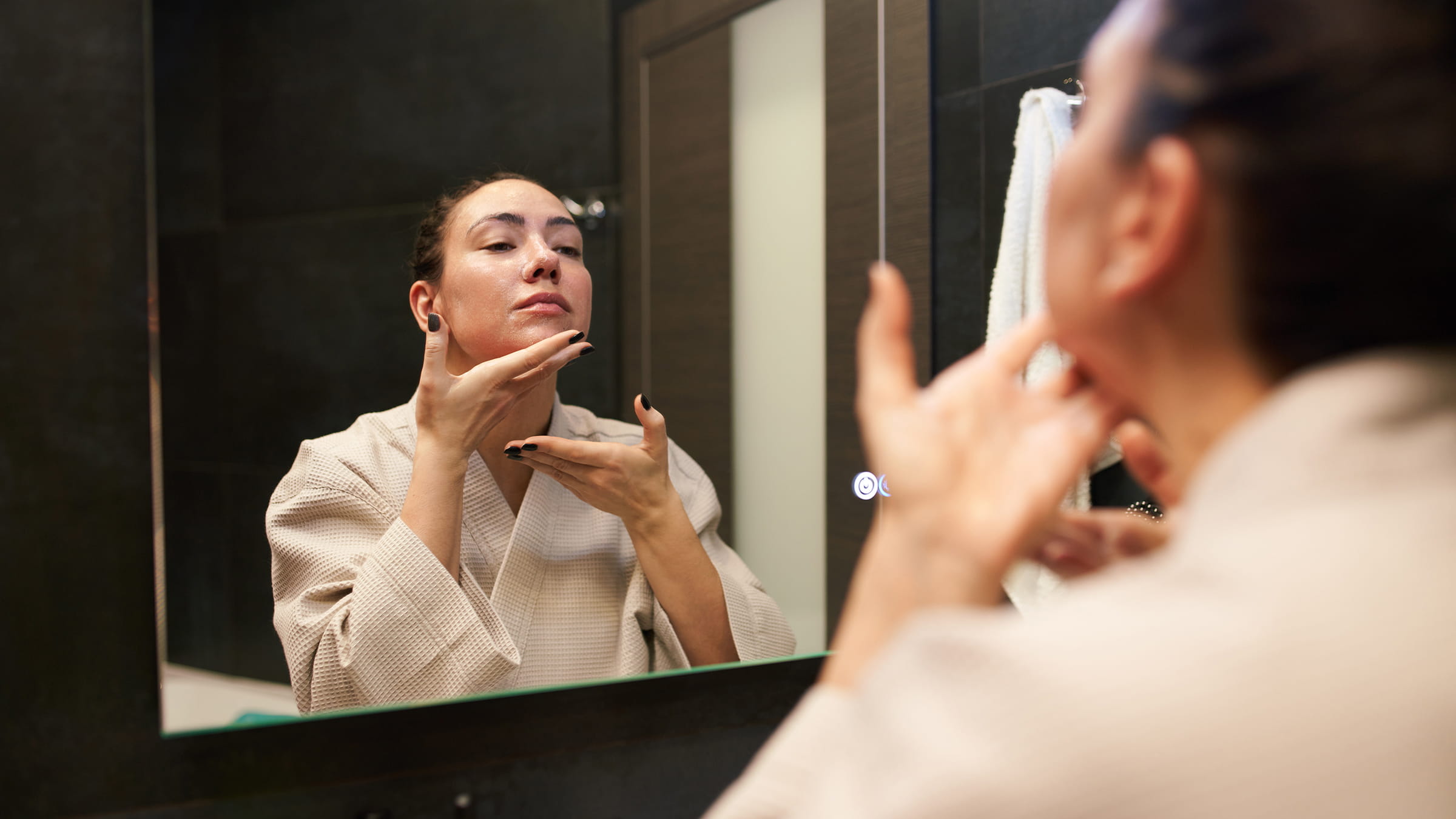 Woman holding chin while looking in mirror.