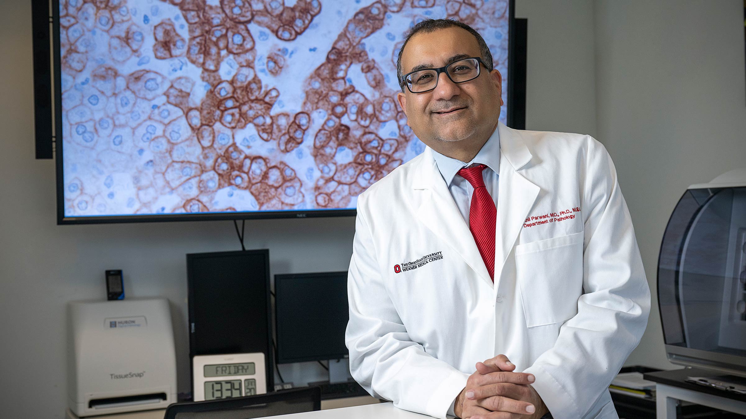 Dr. Anil Parwani standing in front of a screen with a microscopic view of cancer cells