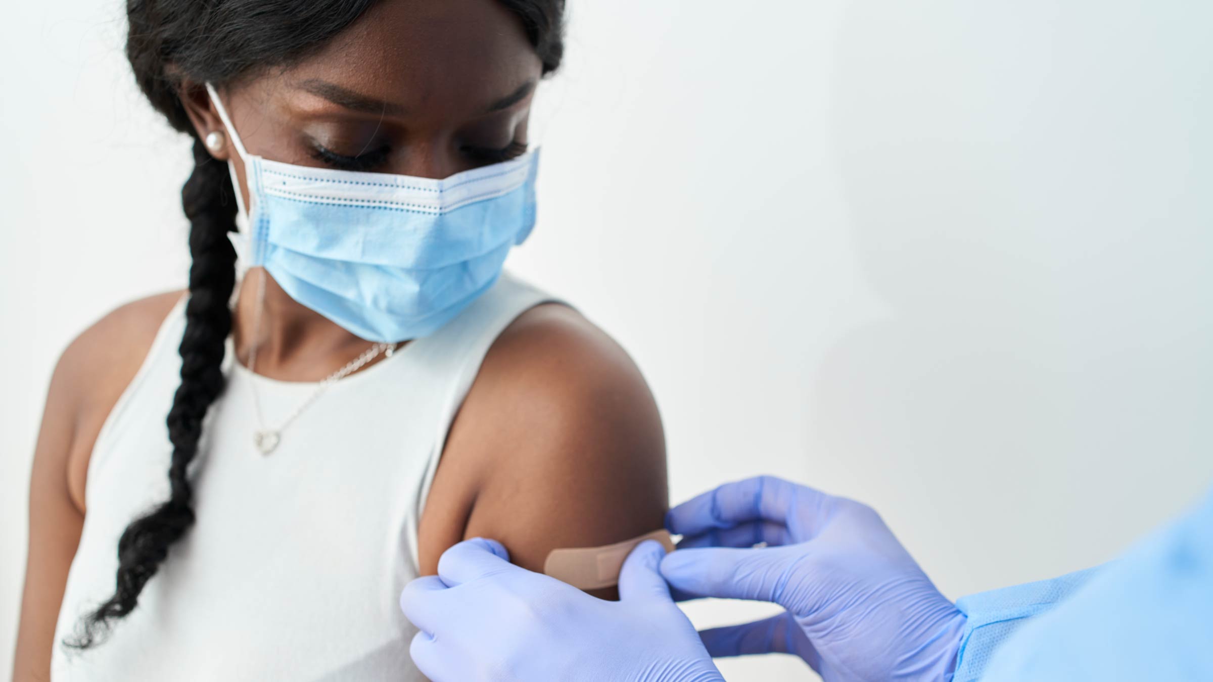 Medical professional putting adhesive bandage on woman's arm after vaccine