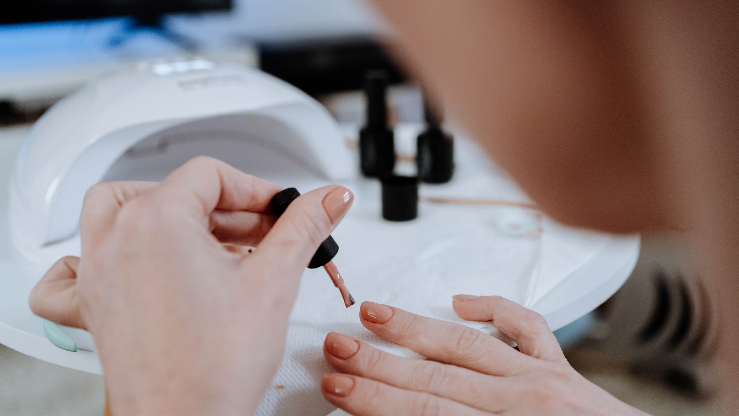 Woman applying gel nail polish before inserting her hand into a UV nail dryer