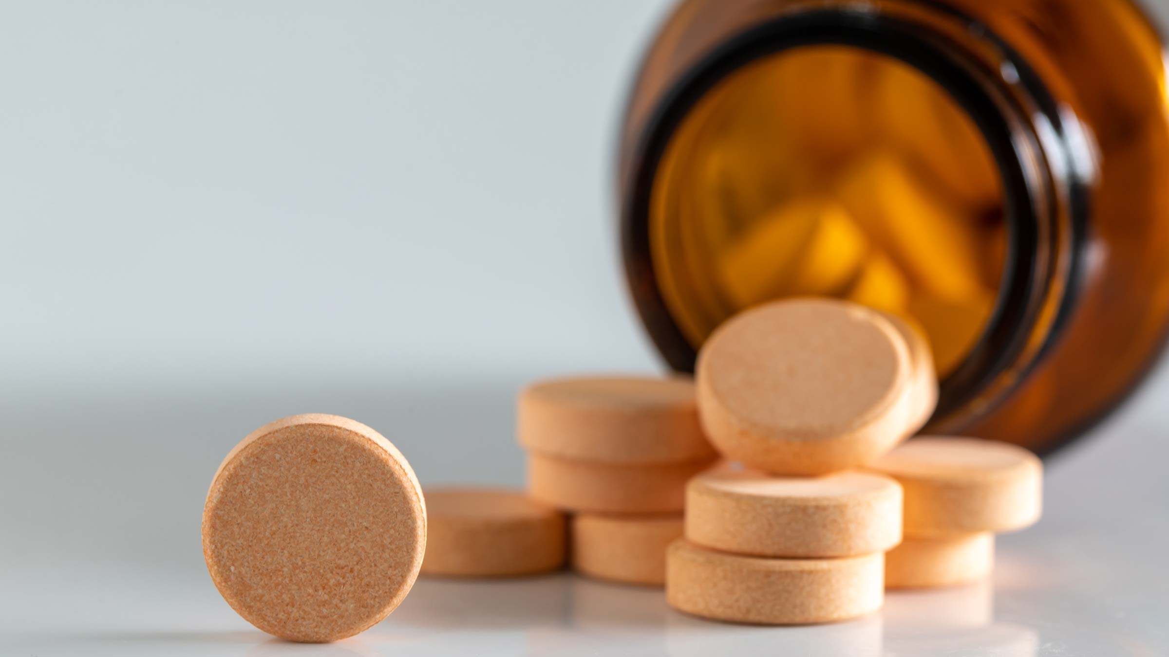 Up close image of vitamin tablets with pill bottle in the background
