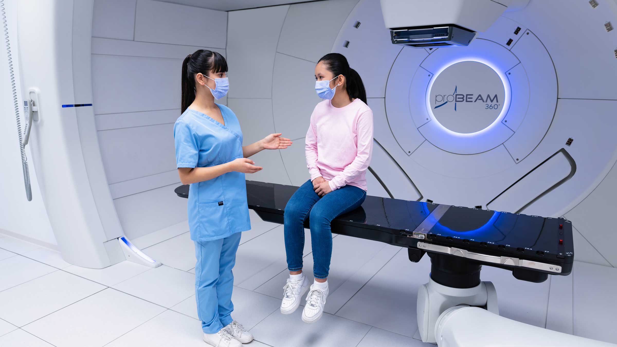 Medical staff member talking with a patient while they sit on the table of the FLASH Proton Therapy machine