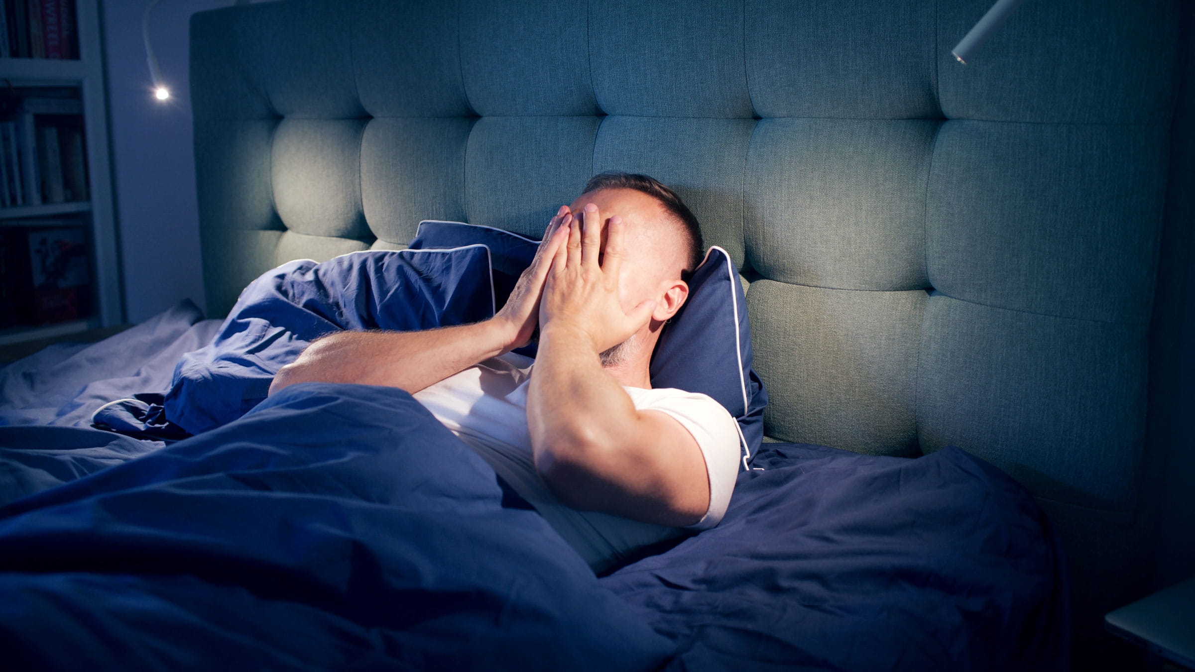 Man in pain lying in bed with his hands covering his face 