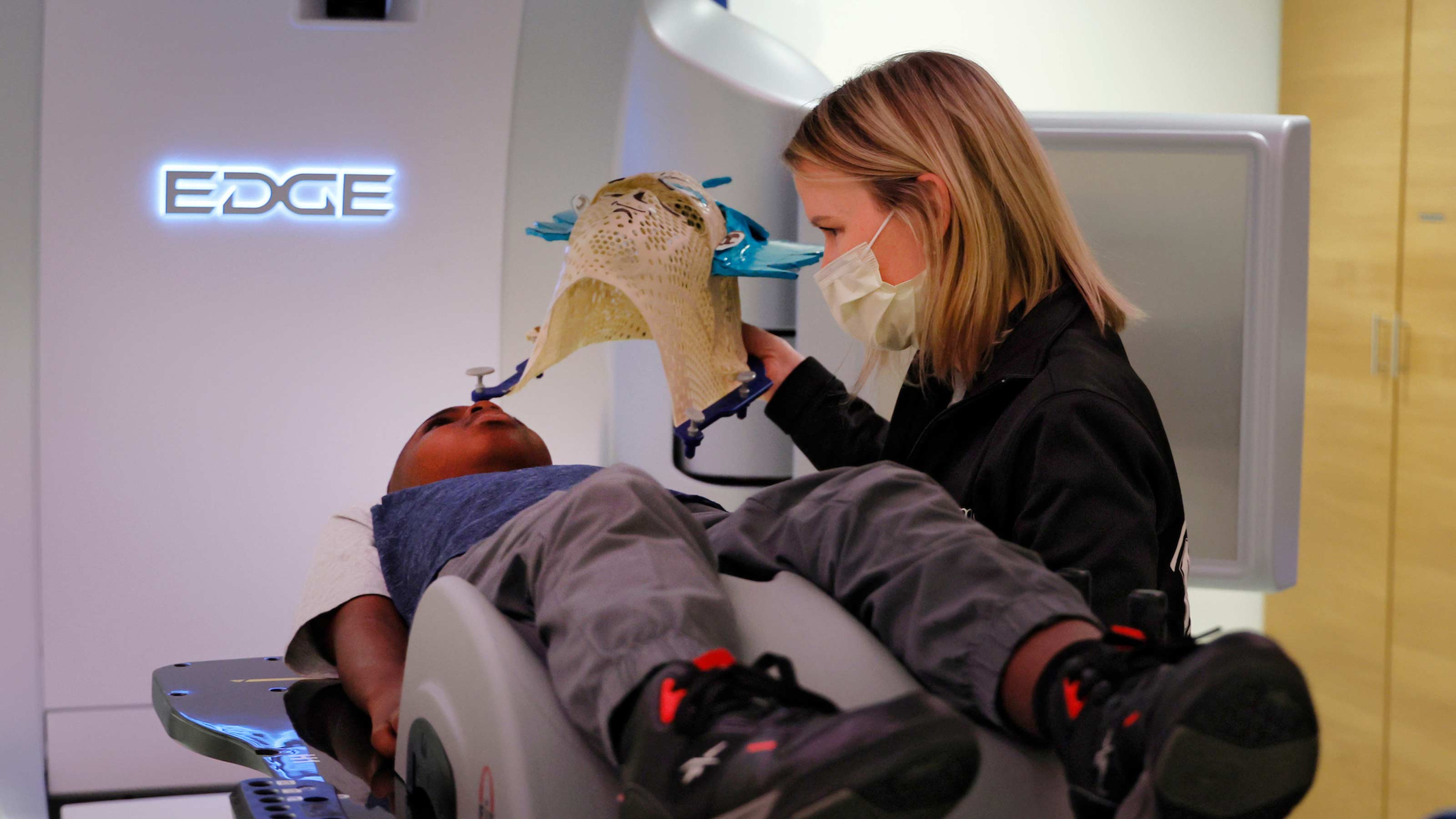 Julie Banner putting a mask on a pediatric cancer patient during treatment