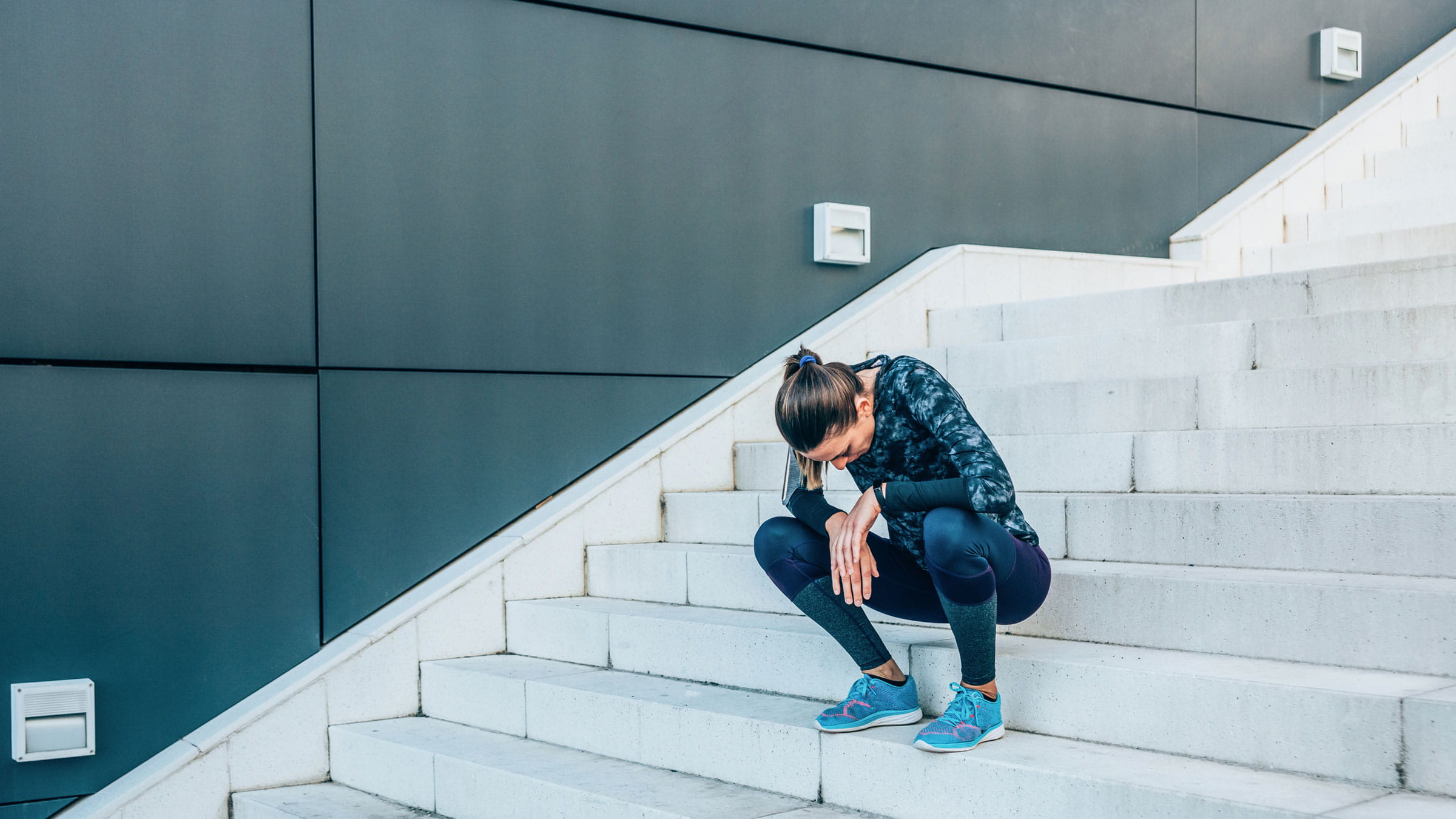 A woman resting on steps after experiencing overexertion from her workout