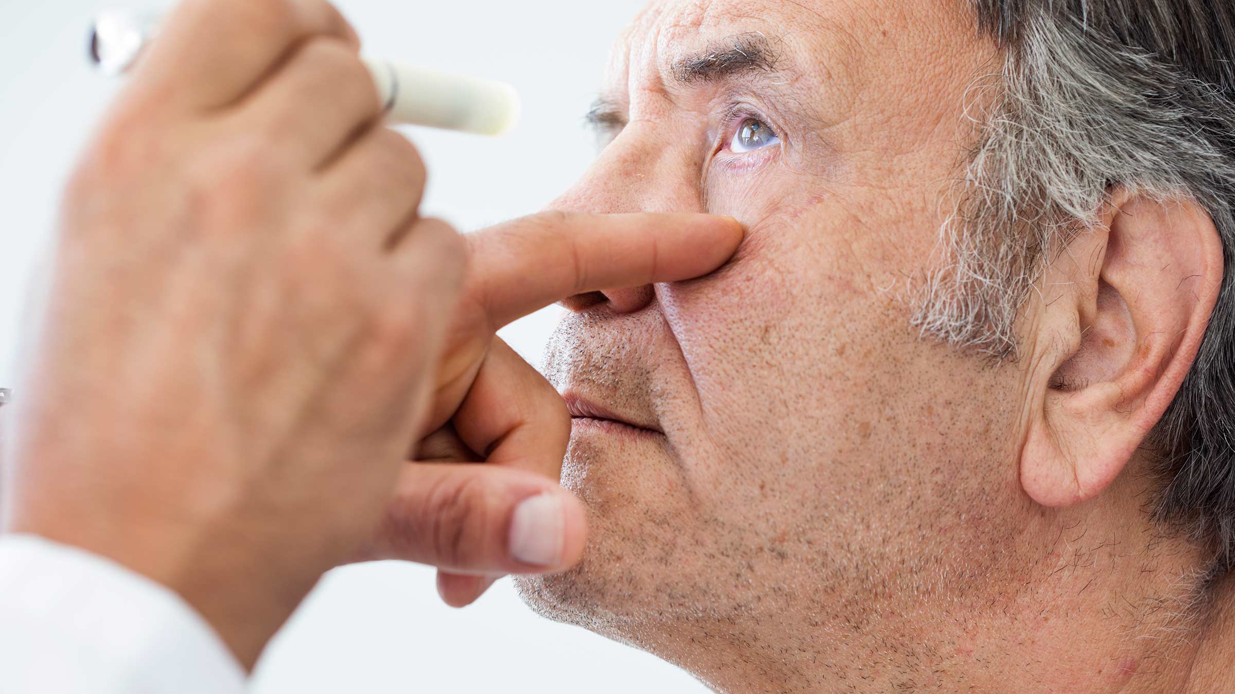 Senior-age man being examined by an eye doctor, who shines a light in one of his eyes