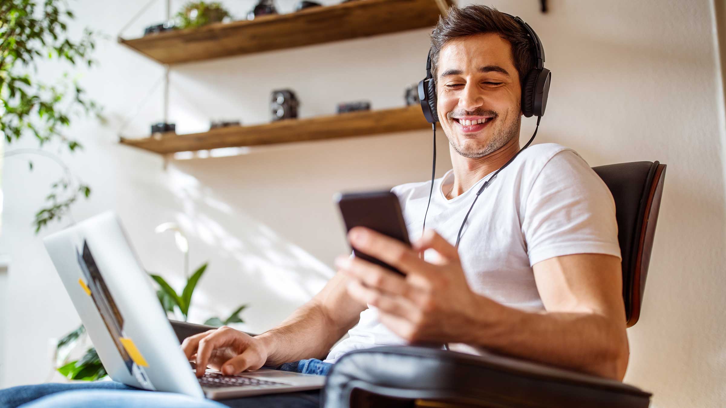 Young adult male using headphones with a laptop and cell phone