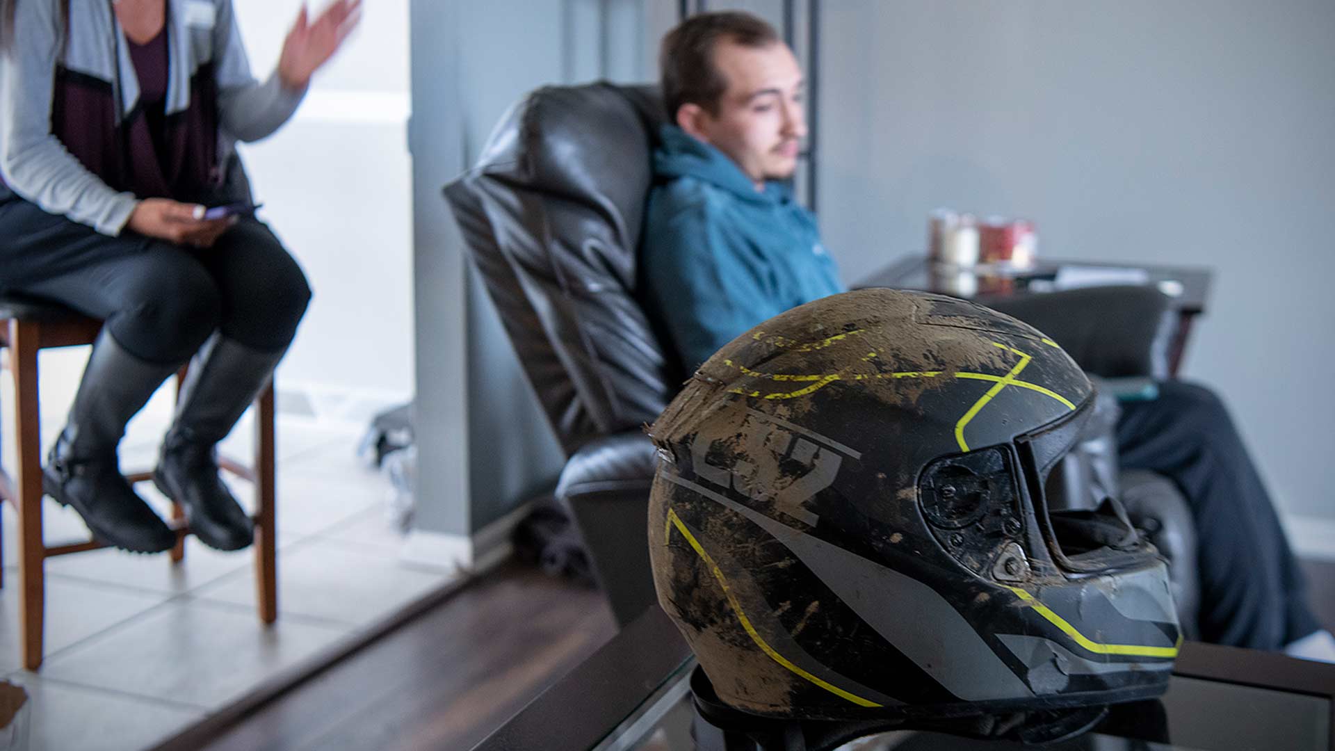 Motorcycle helmet covered in dirt with Cameron in the background