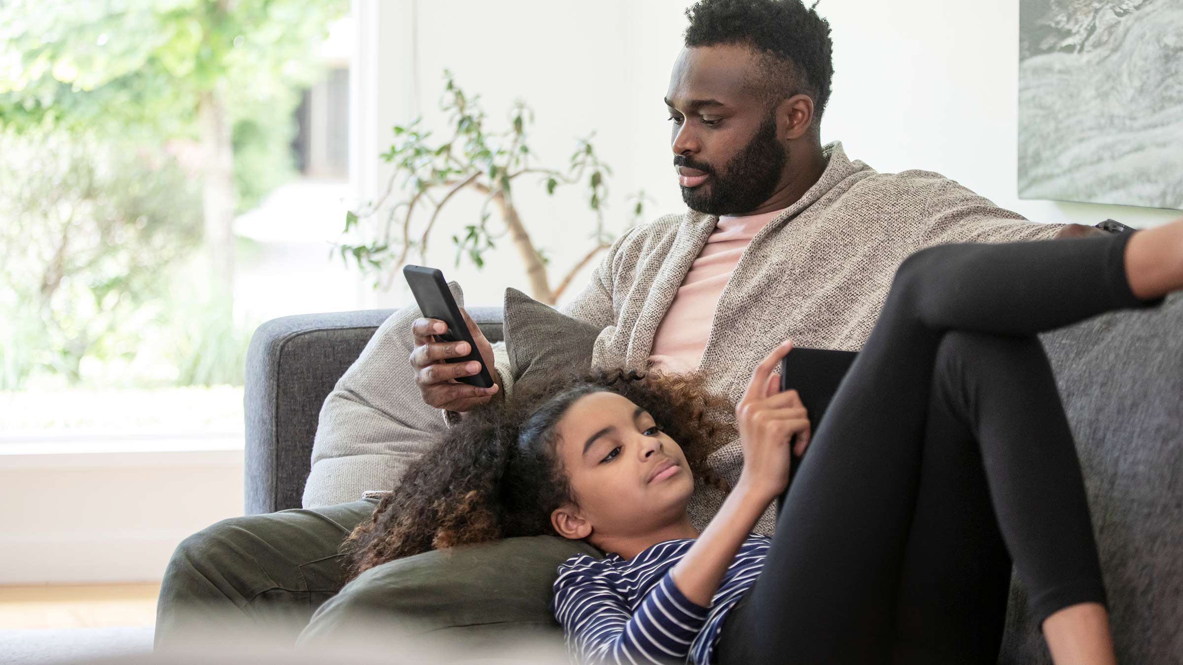 Father and daughter sitting on a couch looking at their phones