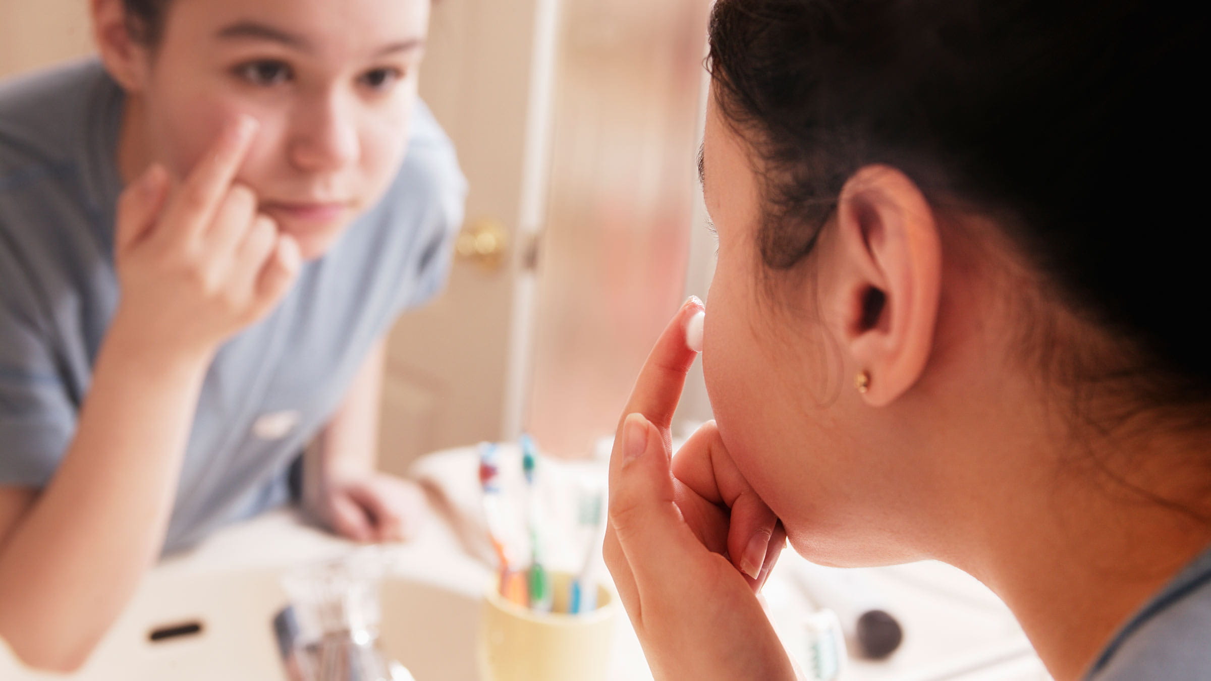 Teen applies facial cream looking in a bathroom mirror