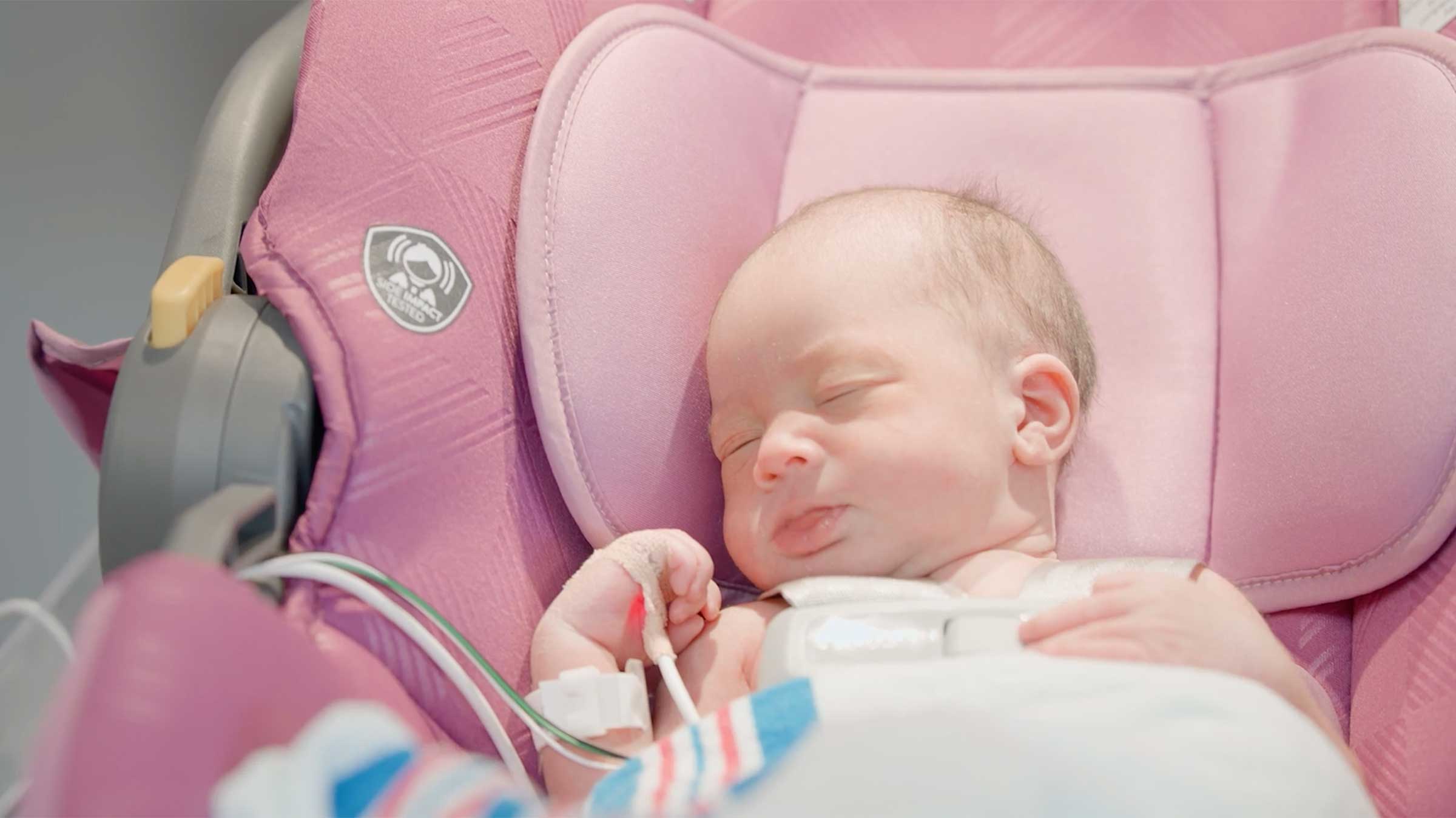 A newborn in a car seat attached to a cardiac monitor