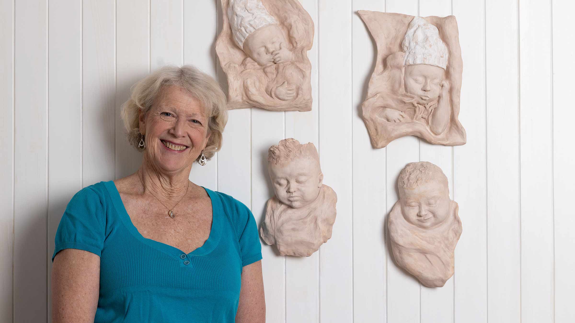 Dr. Maryanna Klatt, smiling and posing with sculptures she made of her grandchildren as babies