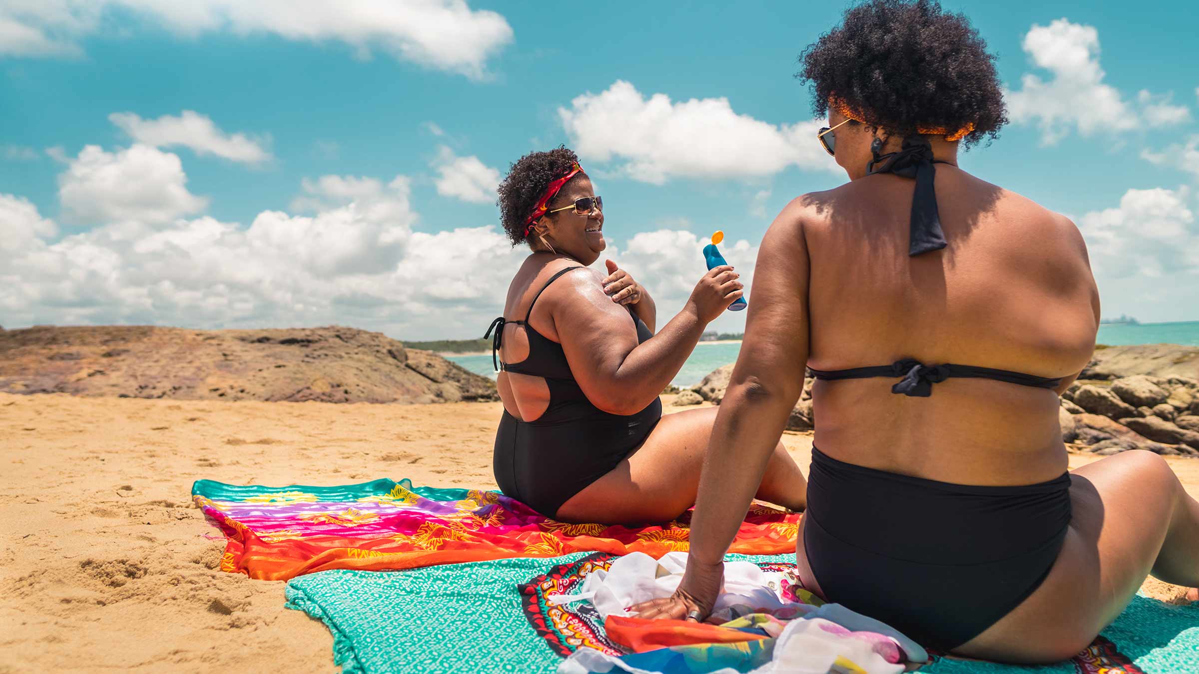 Two women at the beach put on sunscreen