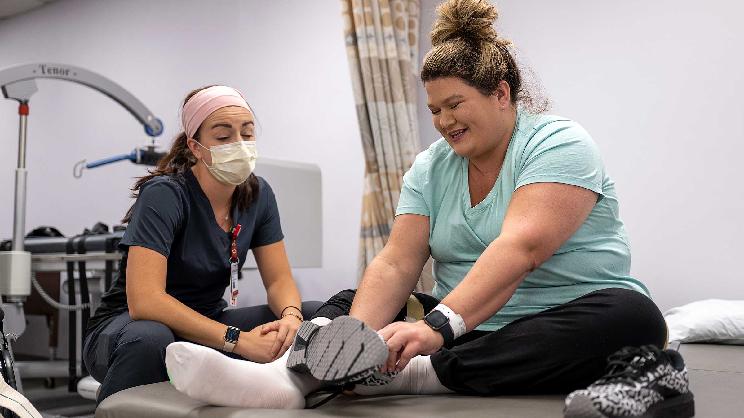 An occupational therapist helps Taylor Haywood practice putting on her shoes