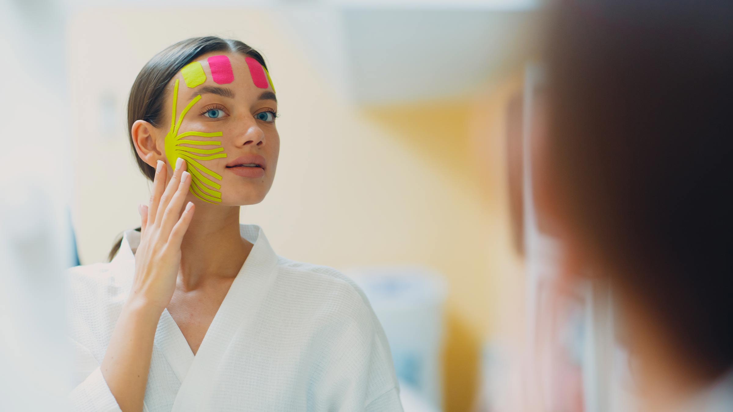 Woman with pieces of tape on her face, looking at he mirror