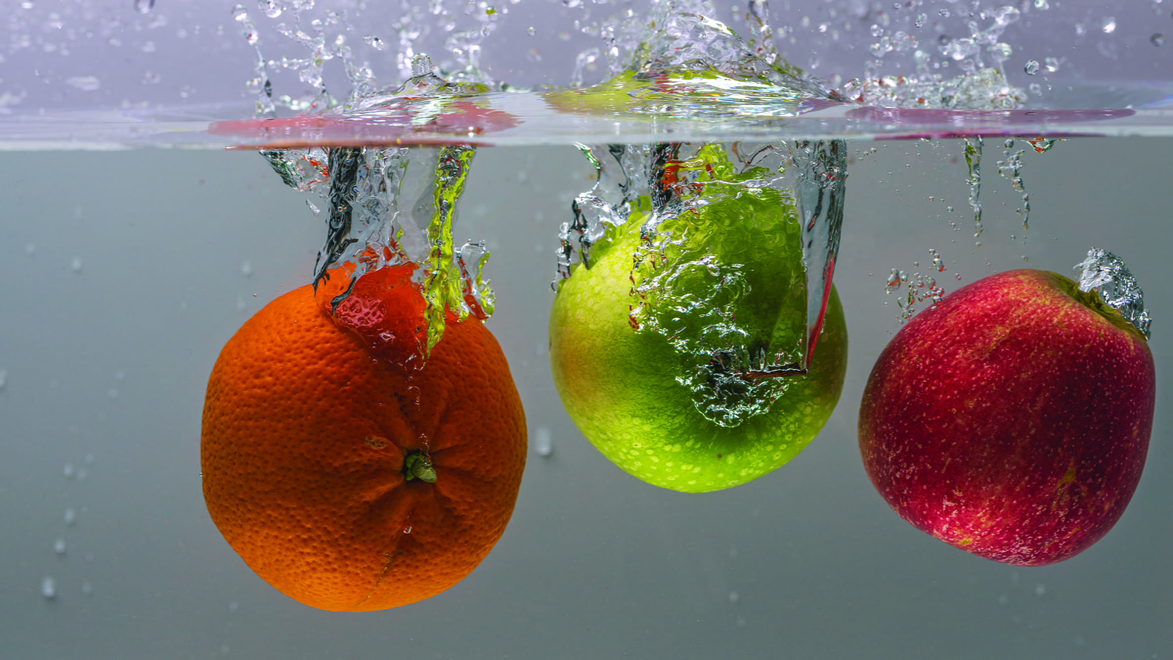 An orange and two apples floating in water 