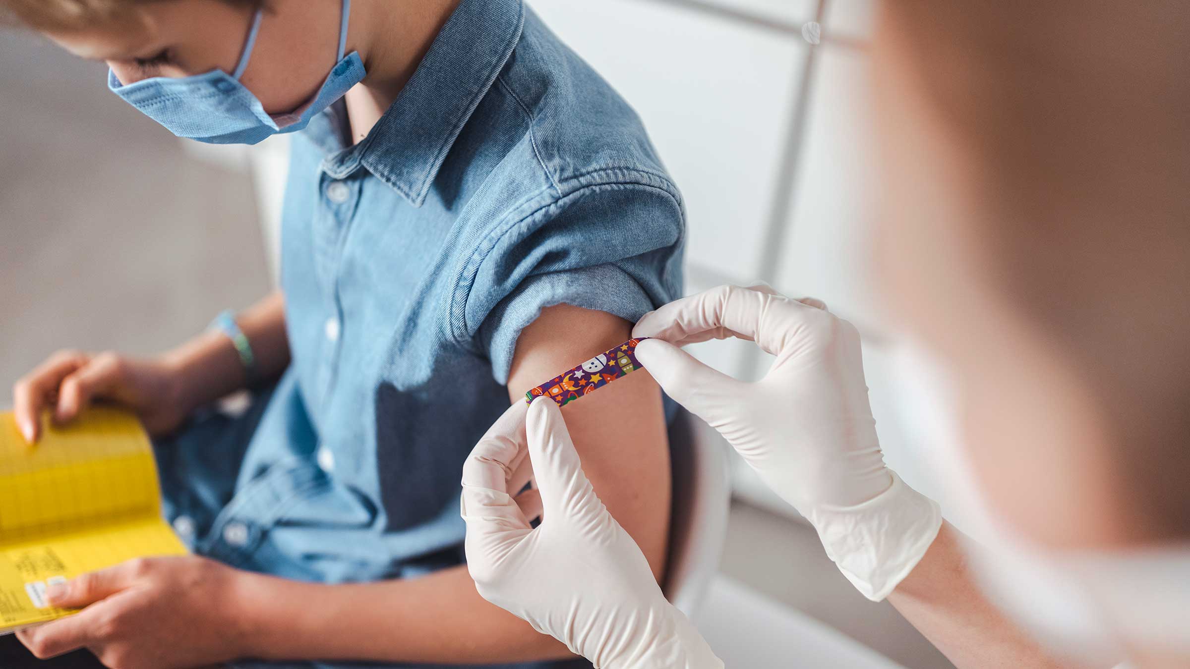 Nurse putting adhesive bandage on a boy's arm after vaccination