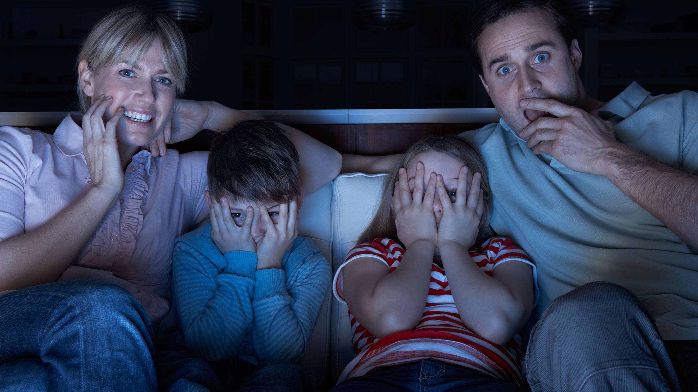 Parents and two children watch a scary movie together from the couch