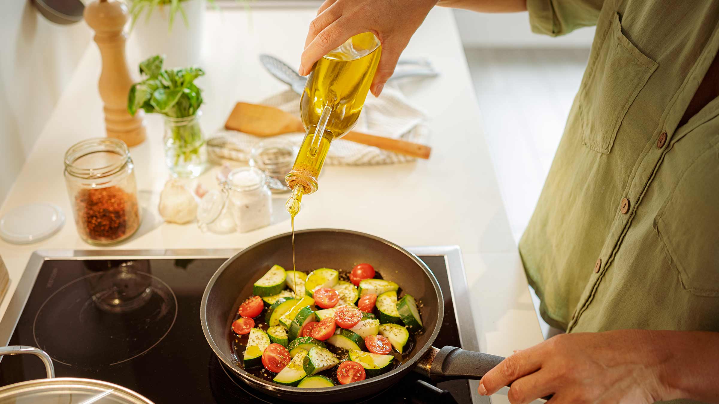 A person pouring oil onto vegetables in a frying pan